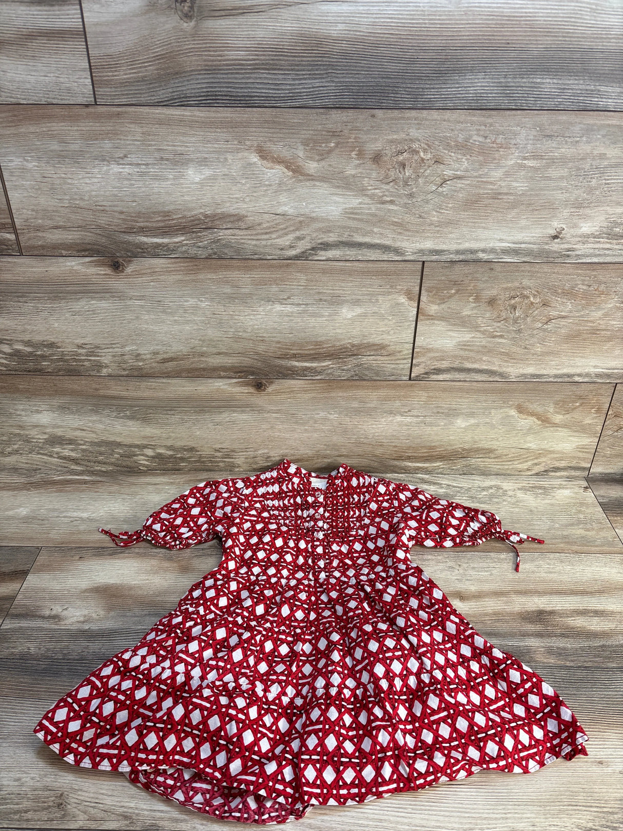 Red and white geometric pattern baby dress with puff sleeves, laid on wood floor