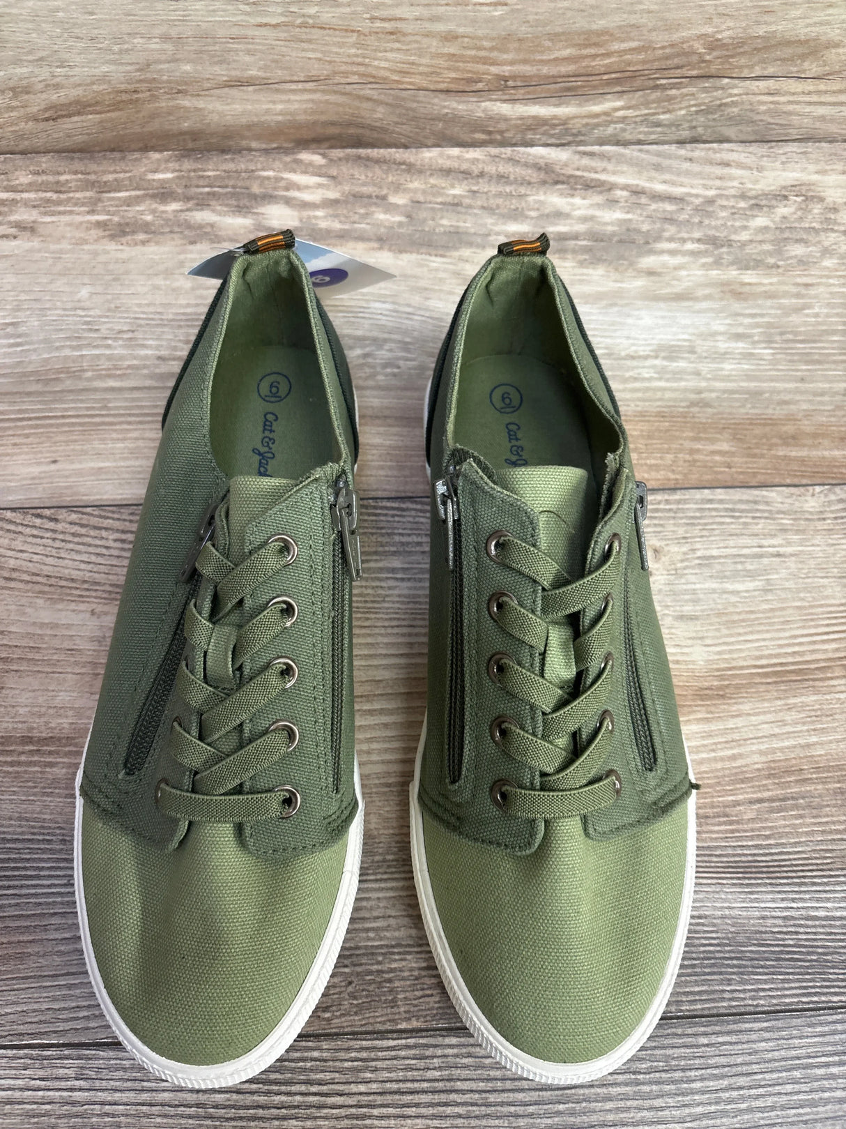 Pair of green canvas kids sneakers with zippers and laces on wooden floor, size 6