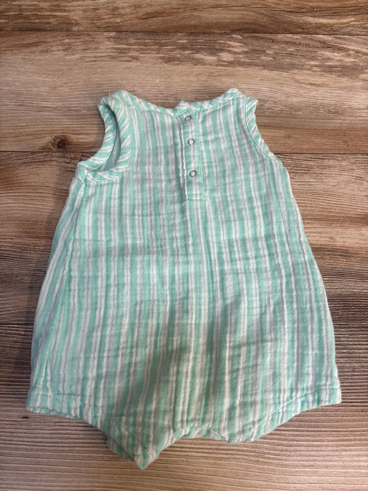 Mint green and white striped sleeveless baby romper with buttons on wood background