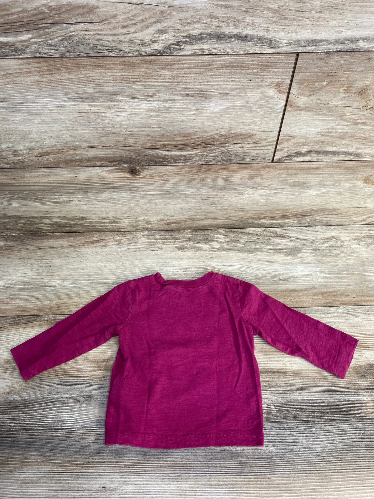 Flat-lay back view of Baby Gap DC Justice League long-sleeve t-shirt in cerise, size 6-12M, on wood floor background