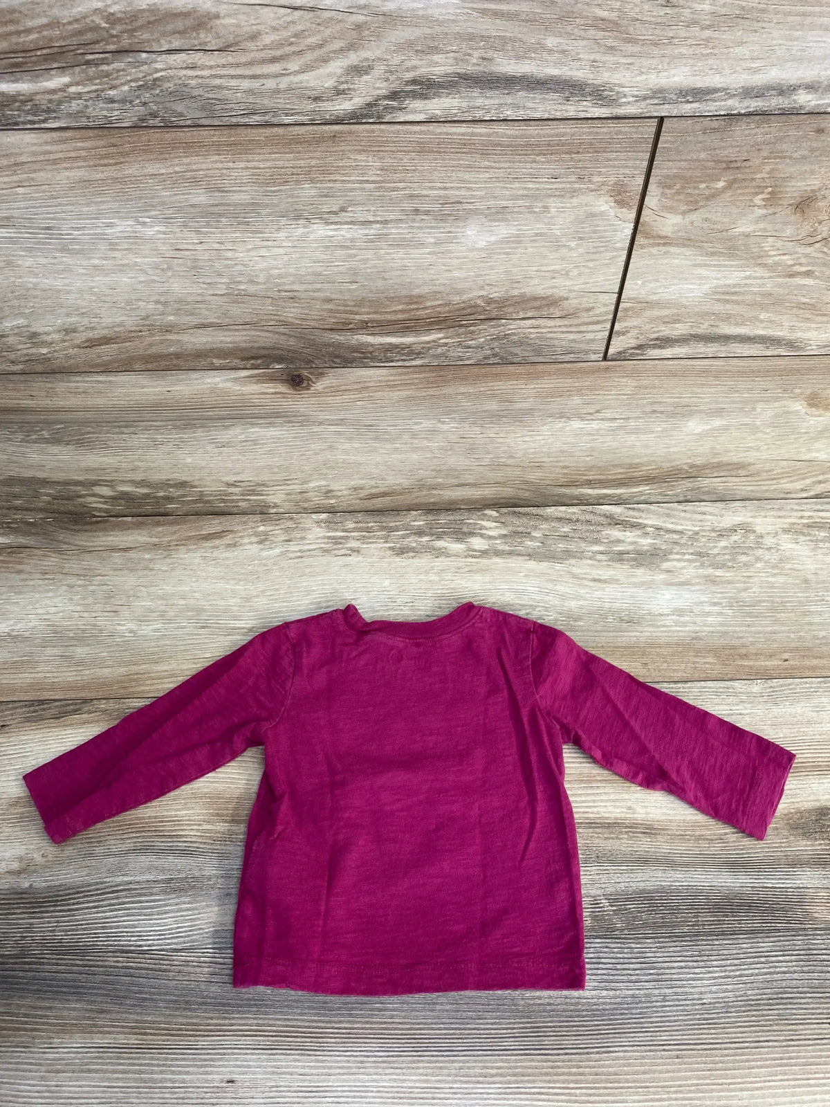 Flat-lay back view of Baby Gap infant long-sleeve T-shirt showcasing plain cerise back with wood floor background, size 6-12M