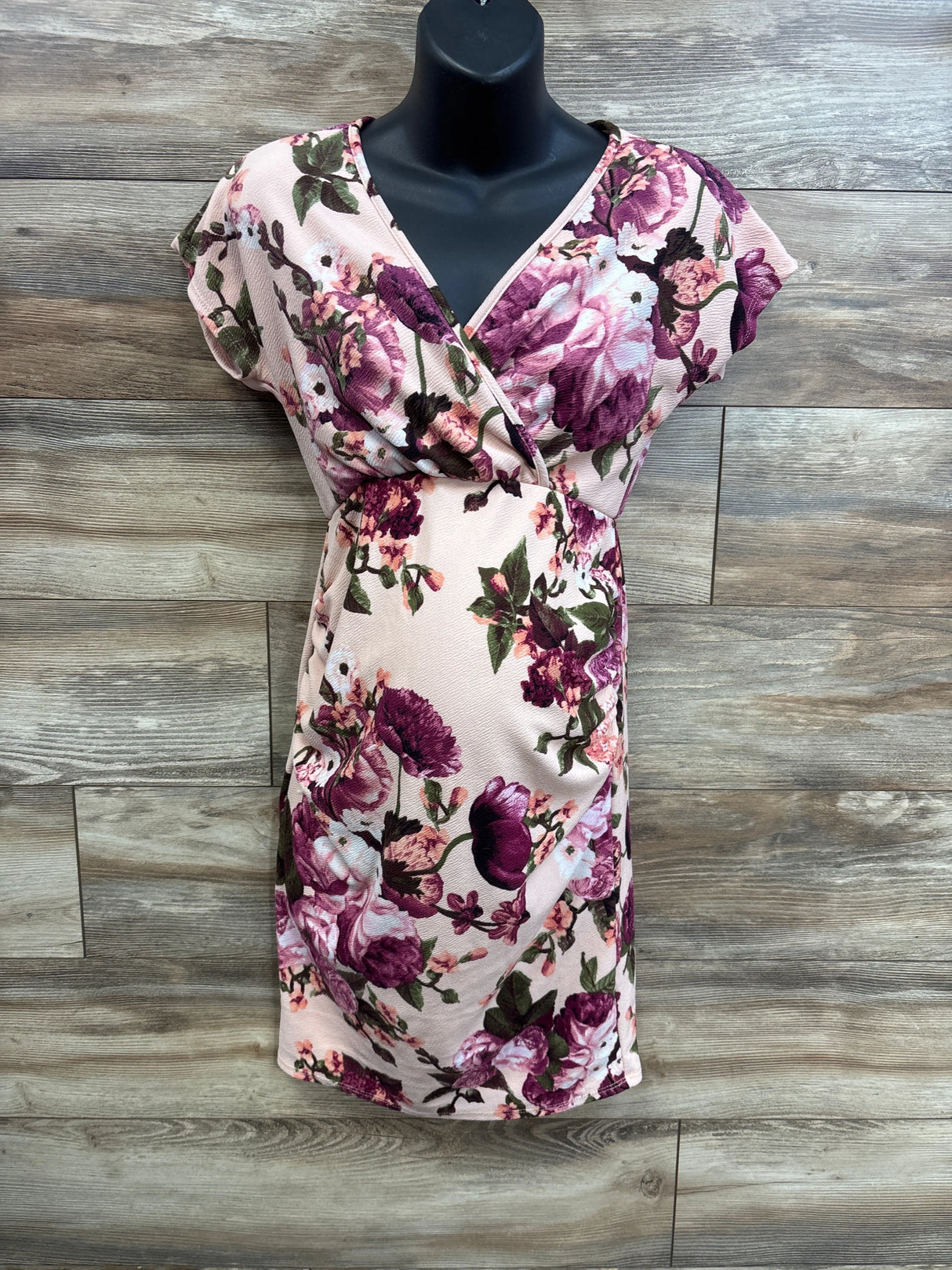 Front view of Pinkblush rose floral wrap maternity dress showing V-neck wrap and fitted belly on wood background