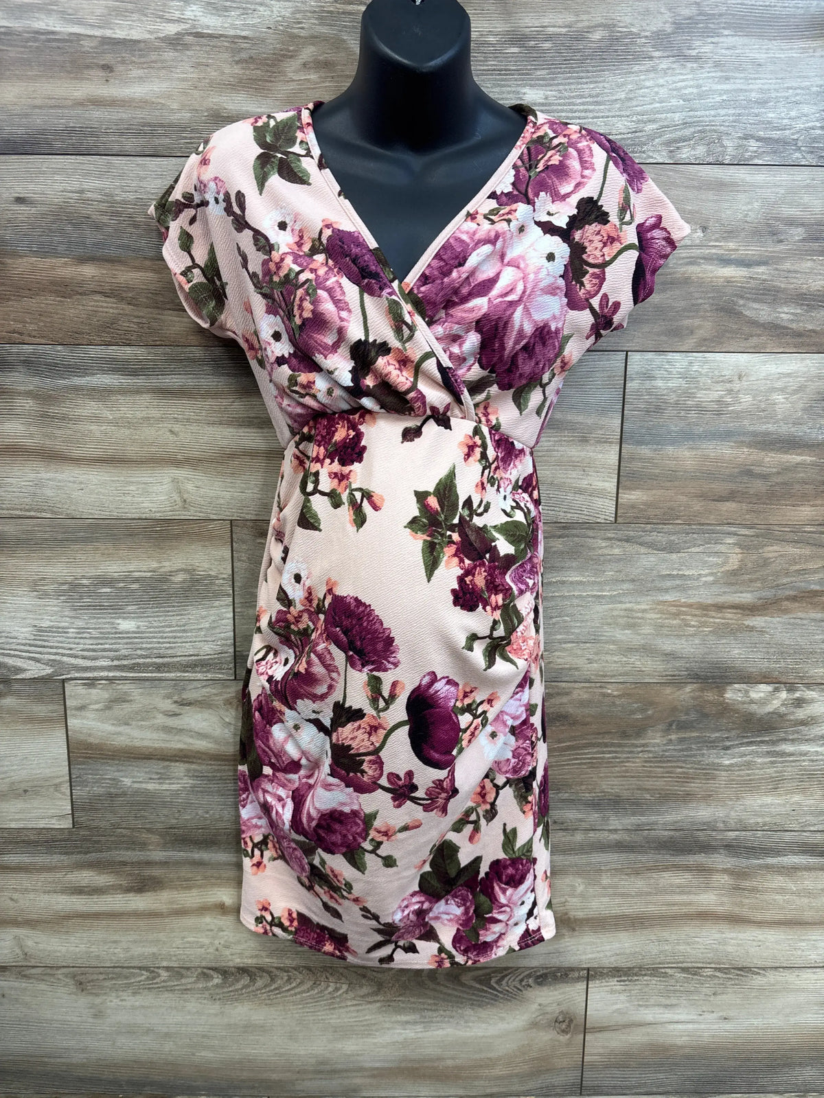 Front view of Pinkblush rose floral wrap maternity dress showing V-neck wrap and fitted belly on wood background
