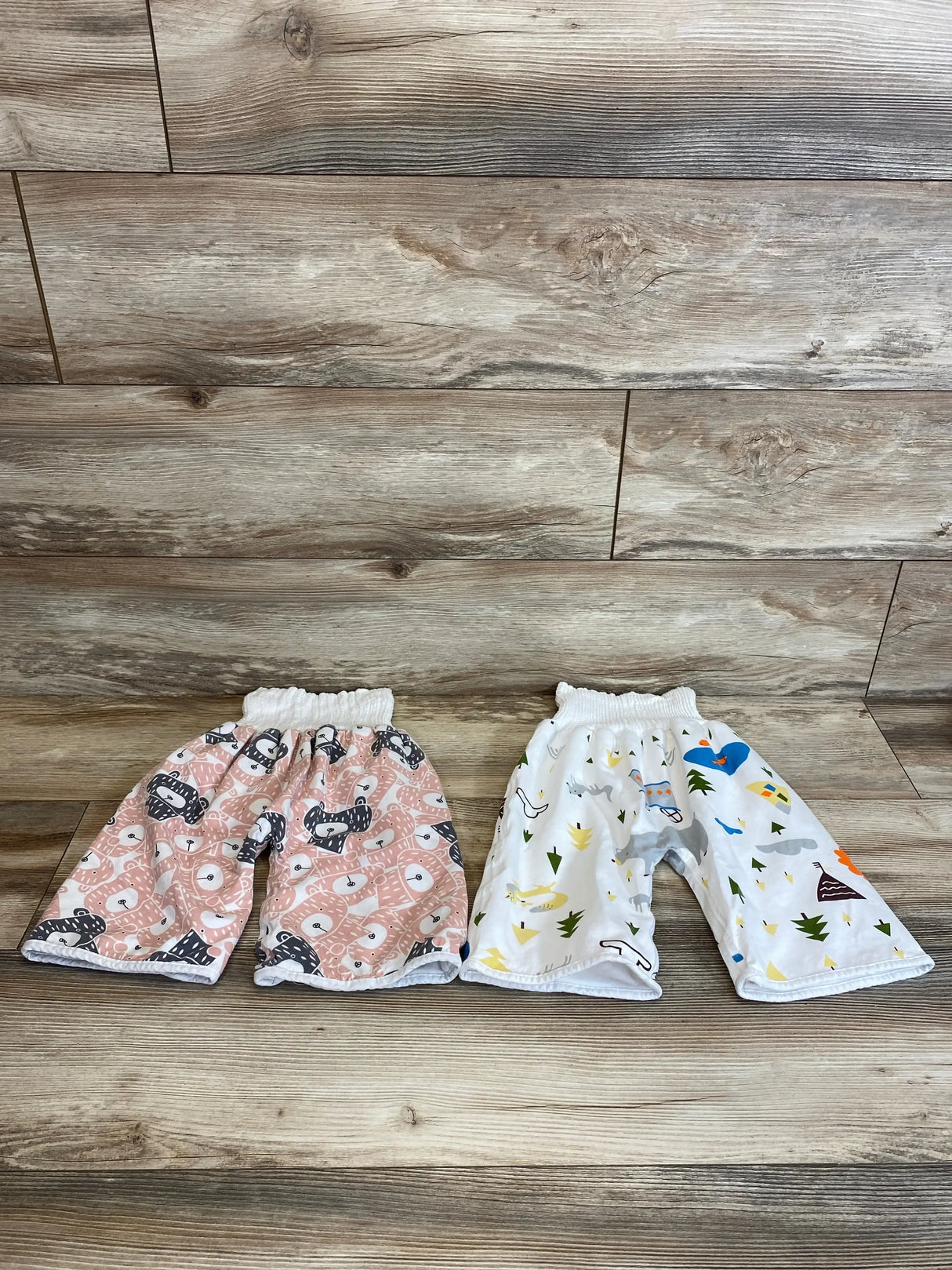 Flat lay of two toddler training pants with elastic waist, pink animal print and white outdoors print on wood background