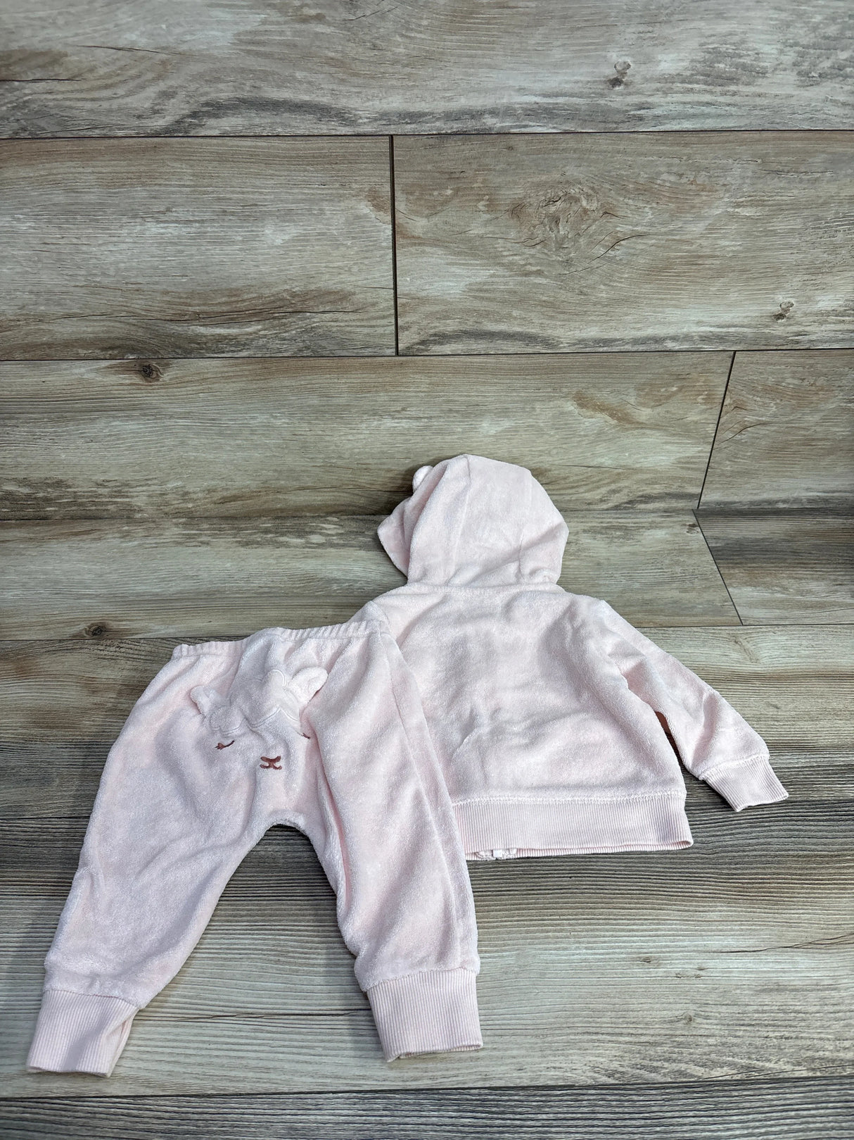 Light pink baby hoodie and pants set with bear face embroidery on wooden background