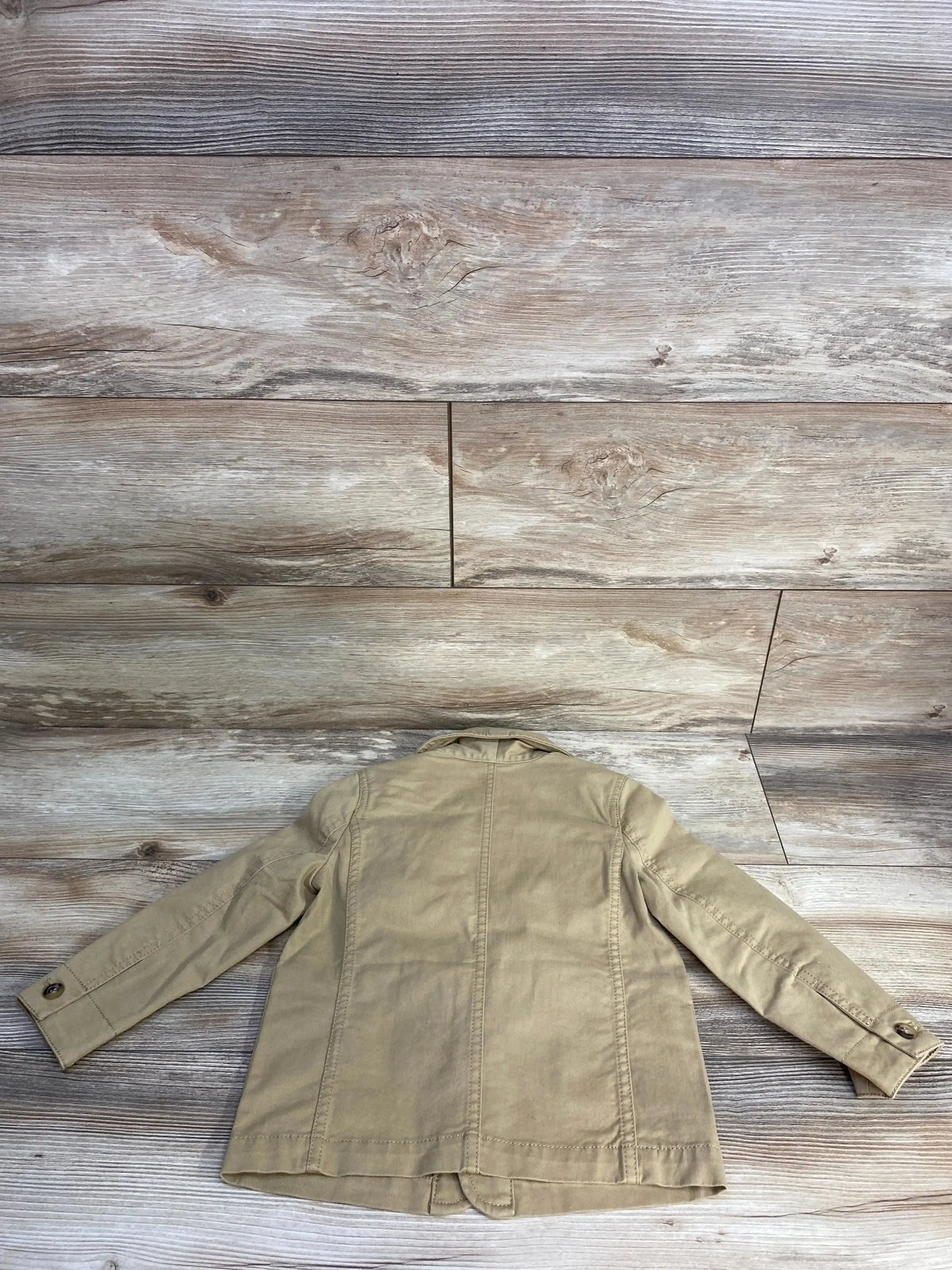 Back view of khaki blazer jacket showcasing center seam buttoned cuffs and structured collar on wood plank floor