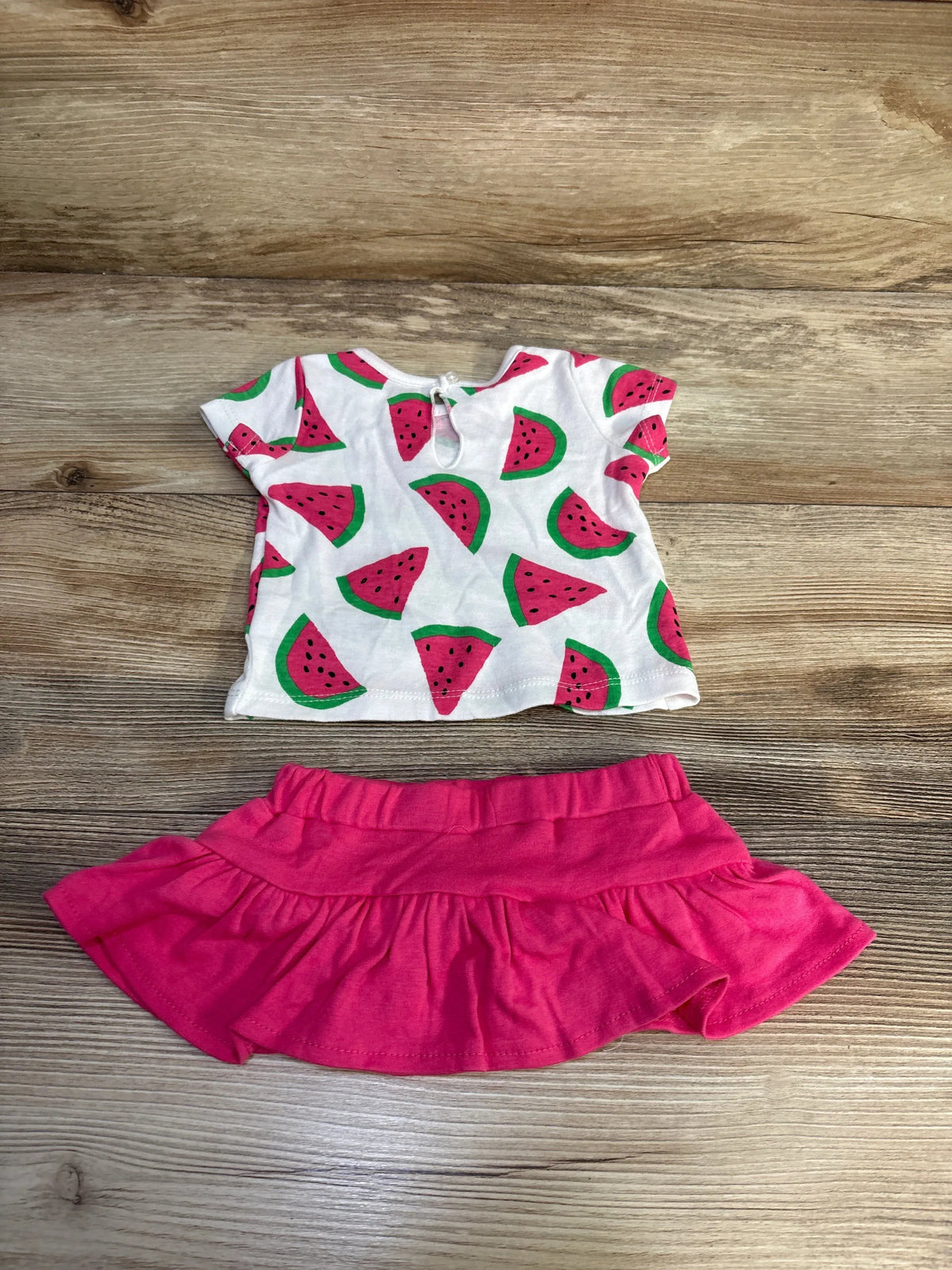 Front view of BWA two-piece watermelon shirt and skort set showcasing watermelon print shirt and pink skort on wood background
