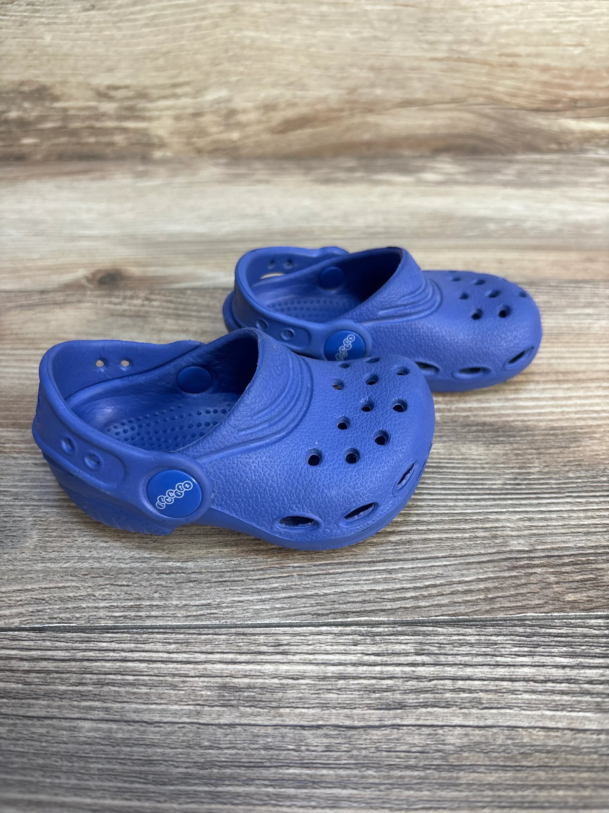 Pair of blue toddler clogs with ventilation holes on wooden surface