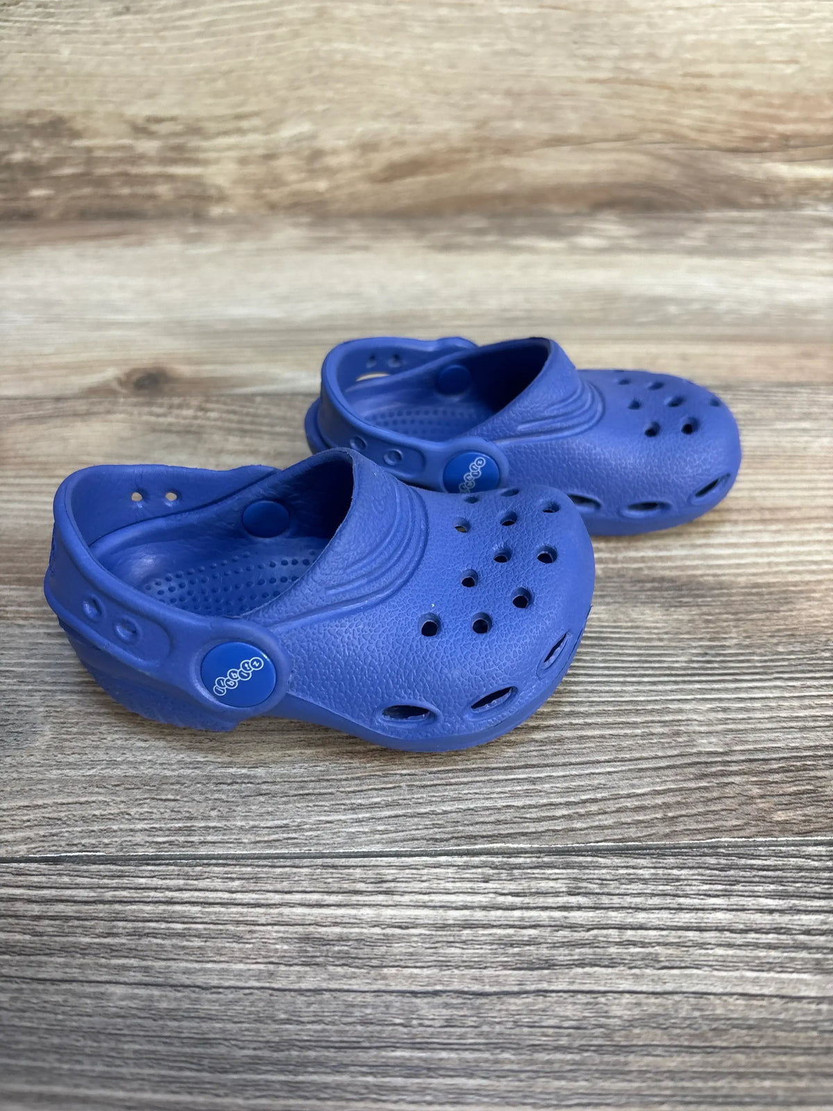 Pair of blue toddler clogs with ventilation holes on wooden surface