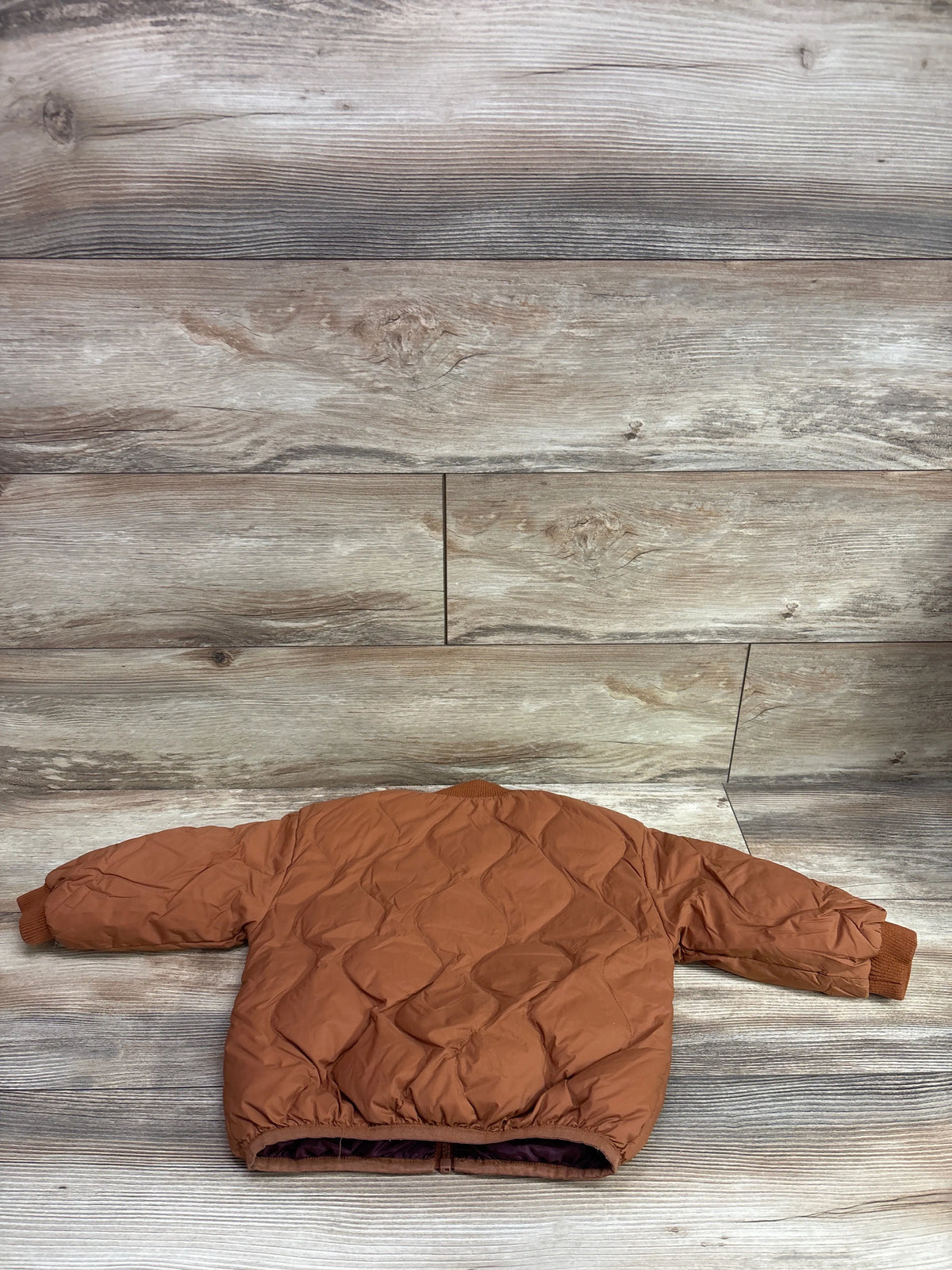 Brown quilted puffer jacket for toddlers laid flat against a rustic wood background.