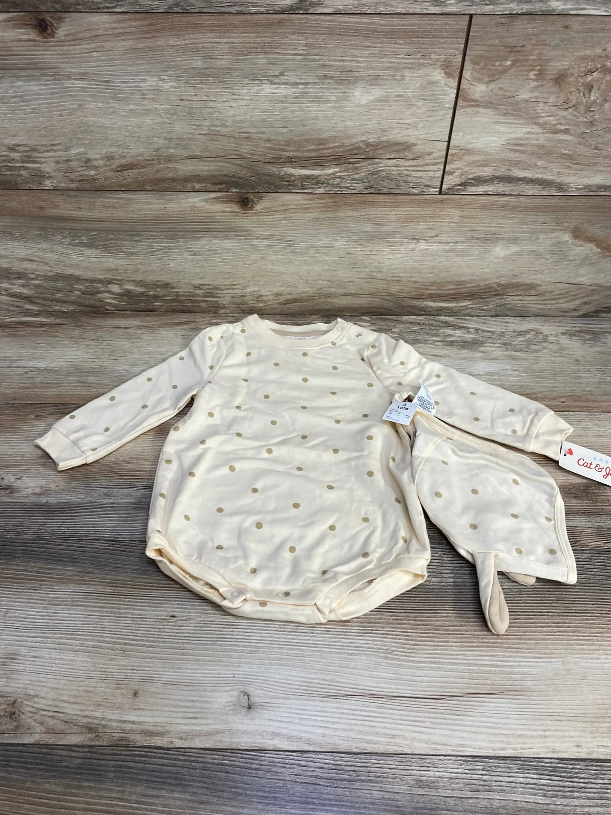 Flat lay of cream polka-dot long-sleeve baby romper and matching bonnet showcasing snap crotch and soft knit fabric on wood background