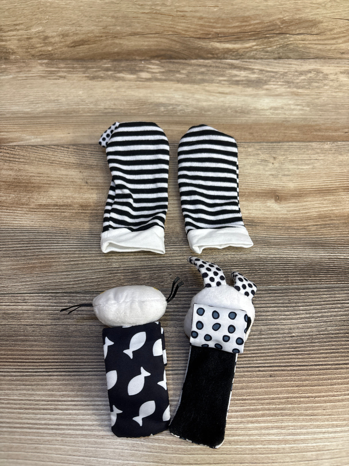 Black and white striped baby mittens and patterned baby rattles on wooden background