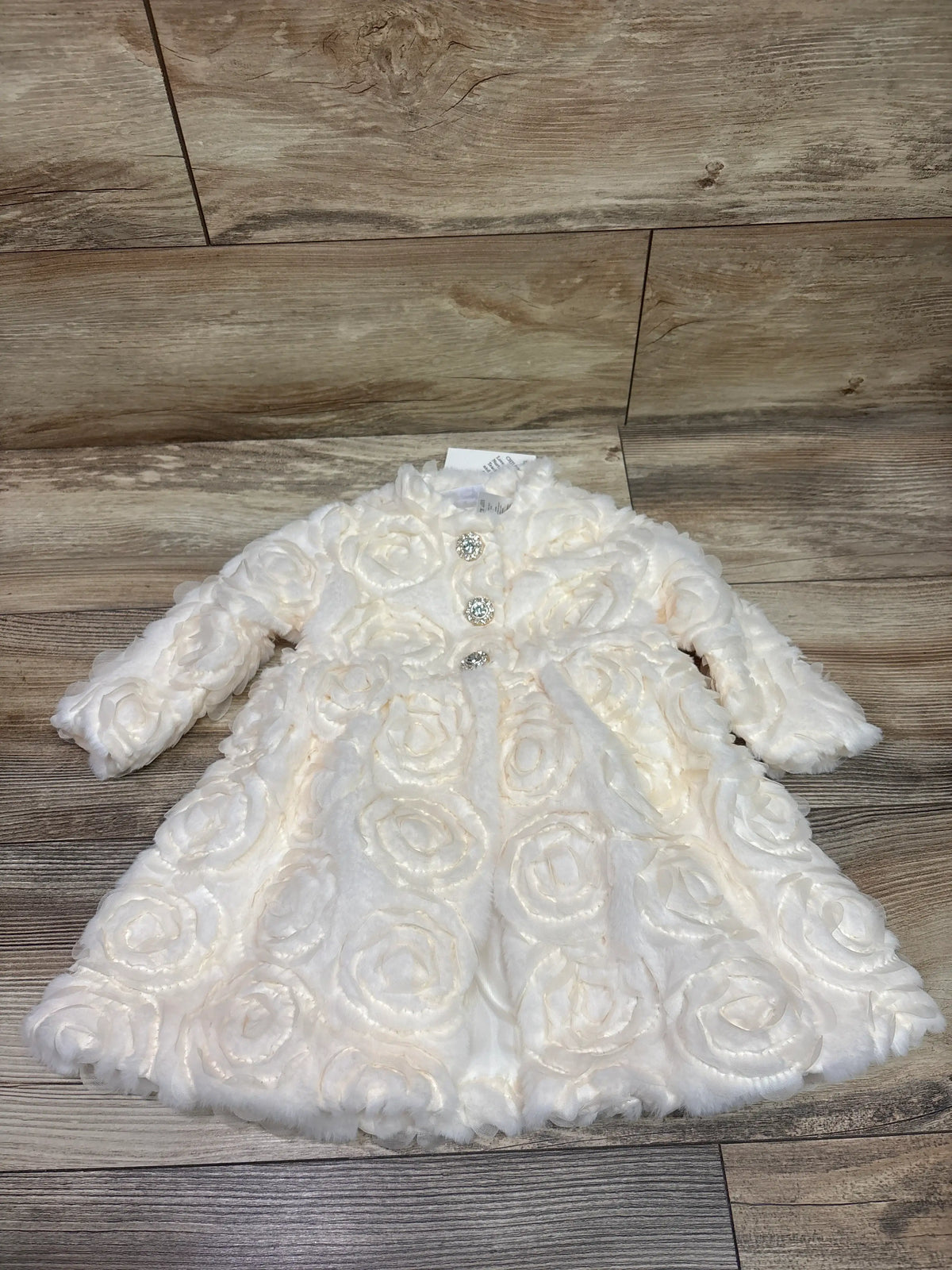 Front view of Blueberi Boulevard ivory rosette dress coat in size 18m, with rosette detailing and jeweled buttons on wood floor