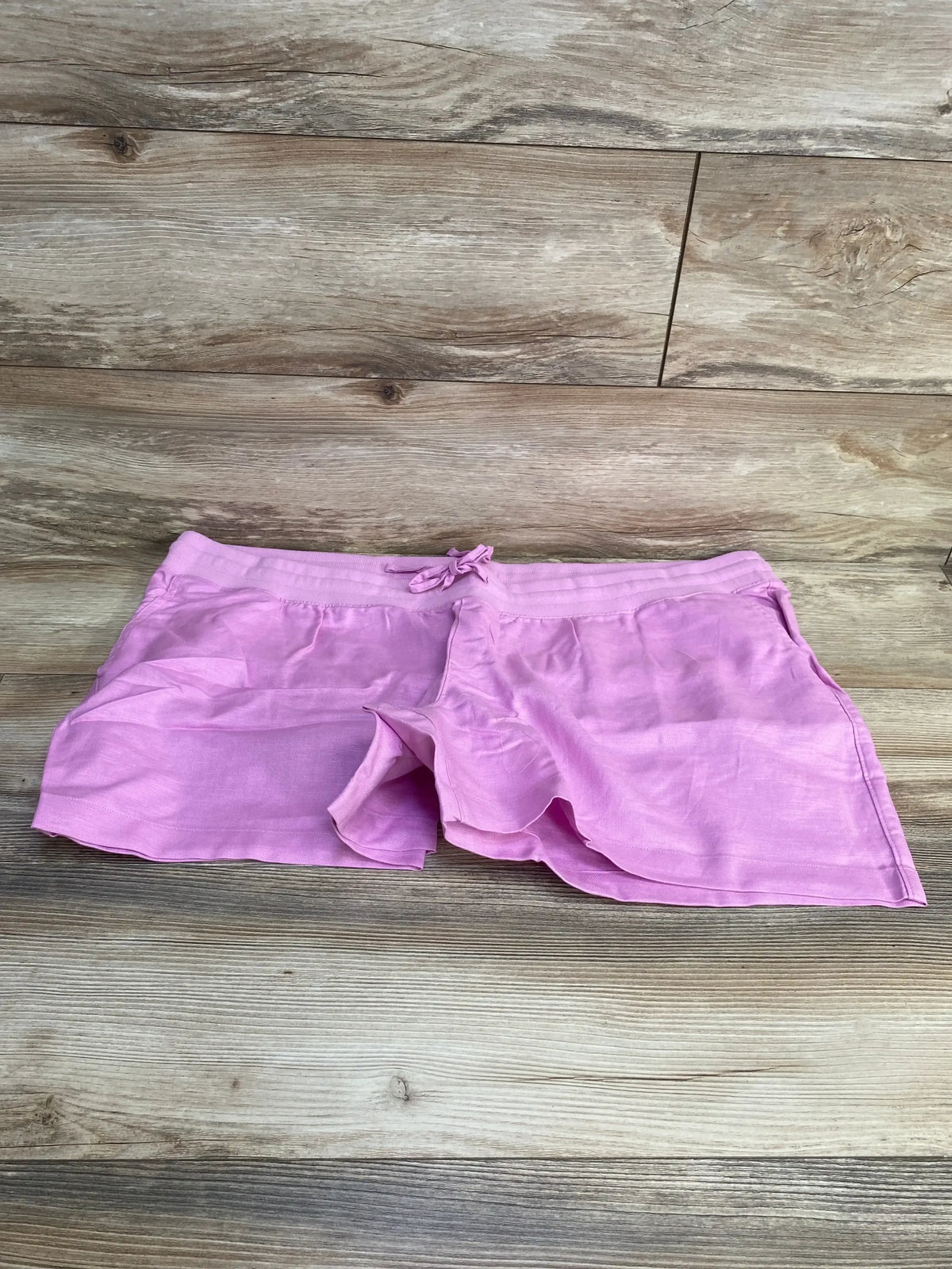 Front flat lay of pink Gap maternity linen-cotton shorts showing elastic drawstring waist and side pockets on wood floor background