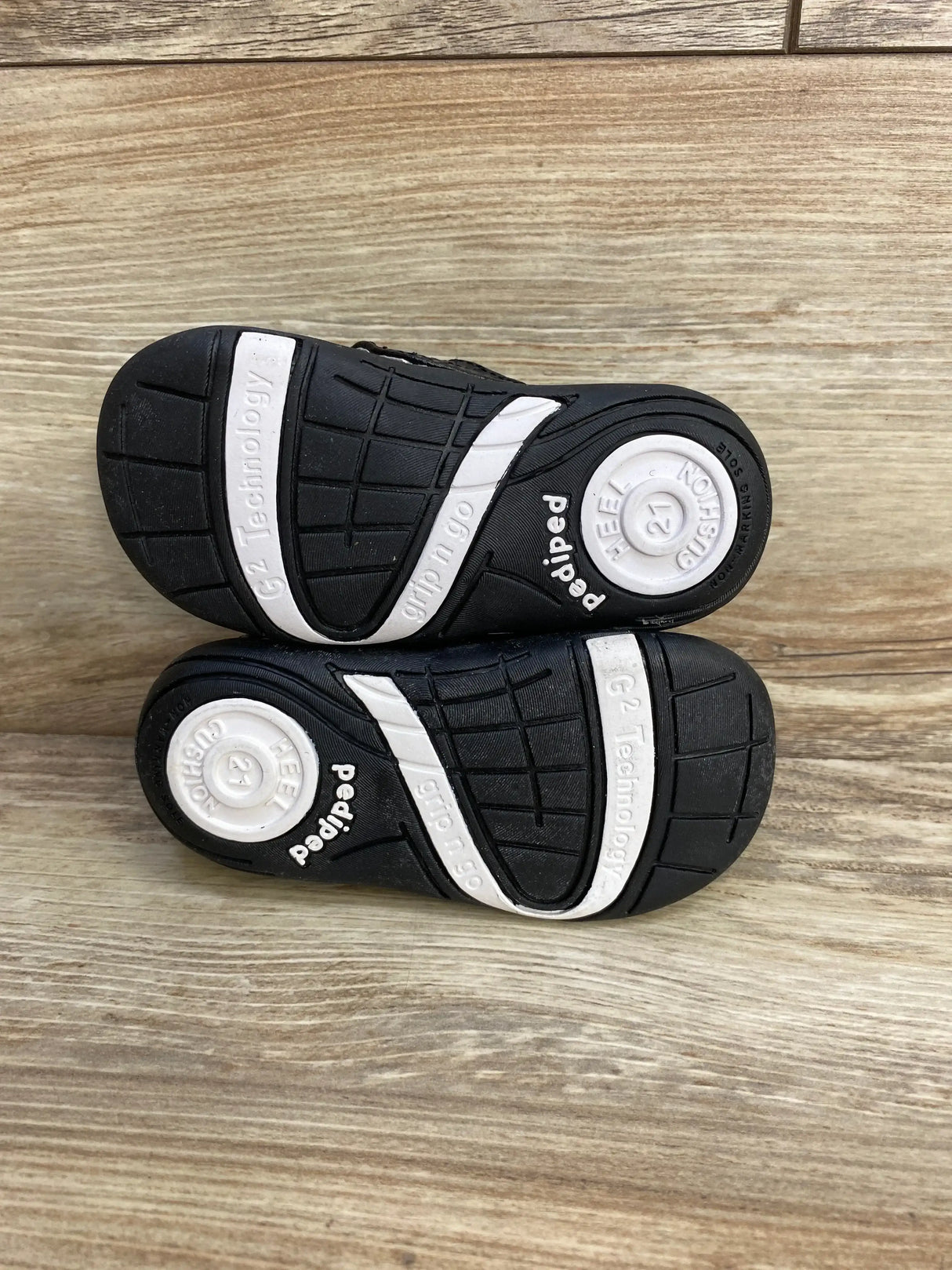 Bottom view of Pediped Charlie baby loafers showing black rubber soles, white heel cushion and size 21 marking on wood background