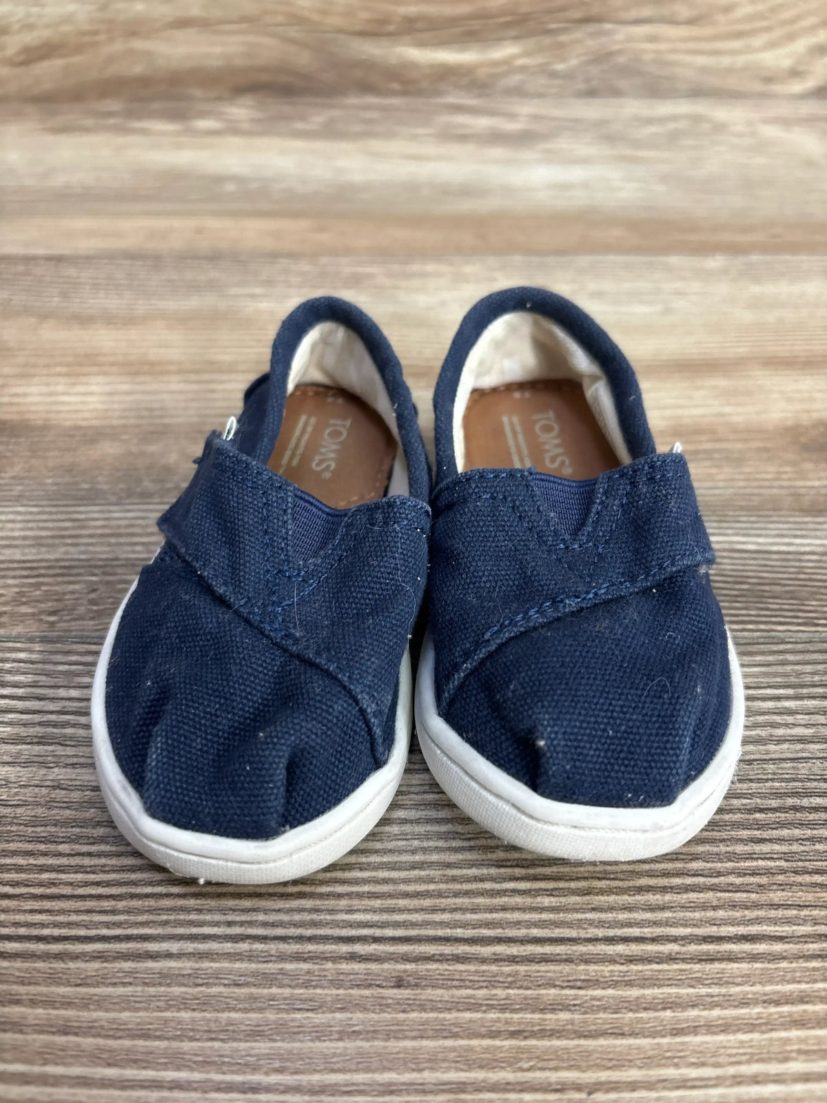 Navy canvas slip-on toddler shoes with white soles on wooden surface