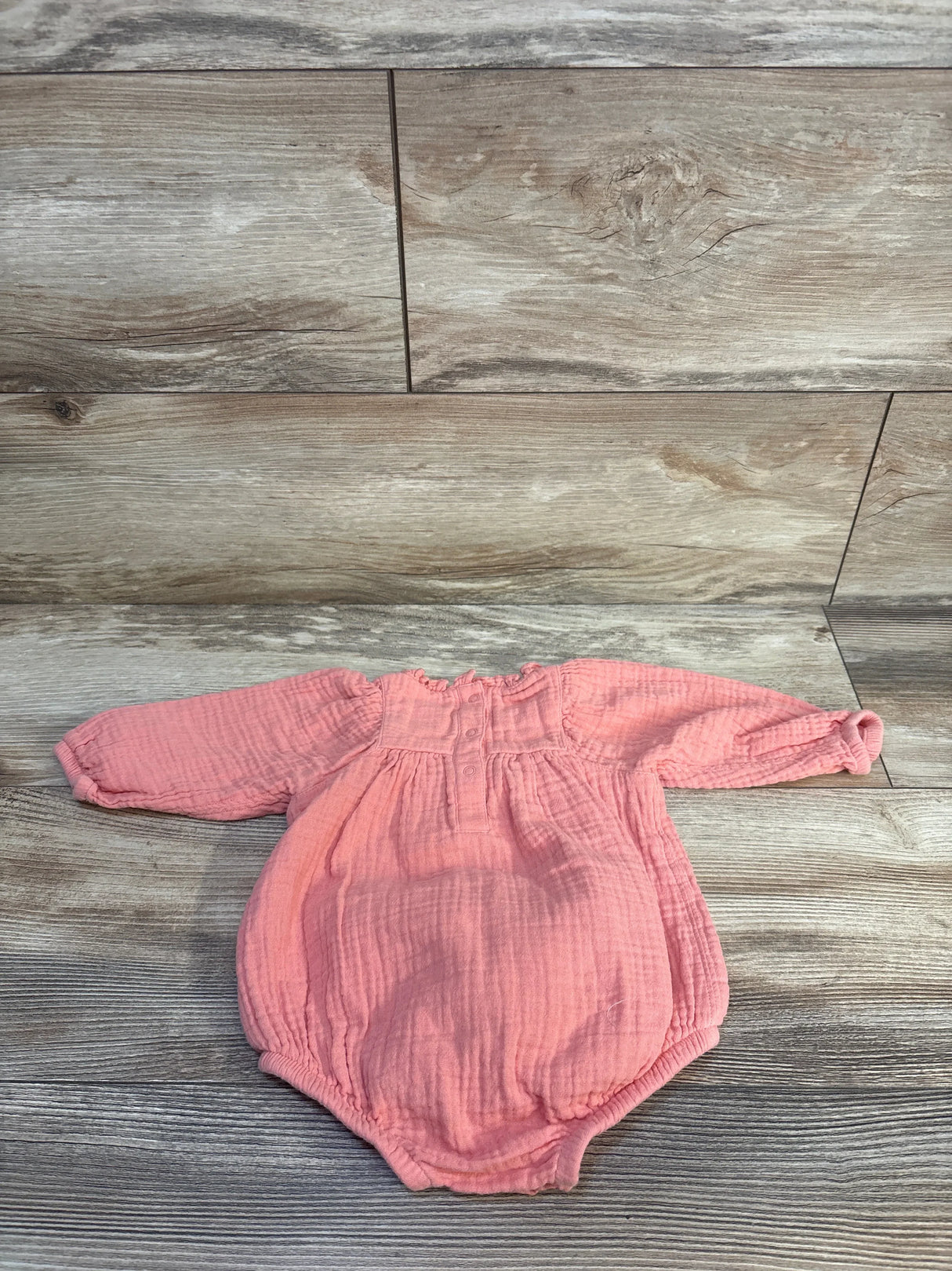 Pink baby onesie with long sleeves and smocked details on wood floor