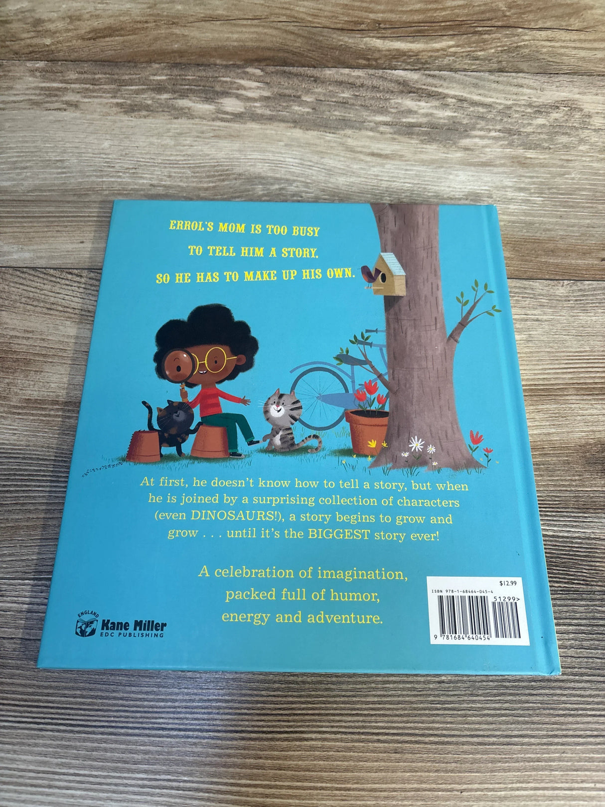 Back cover of The Biggest Story book showing a boy, cat, and raccoon by a tree with yellow headline text on blue background