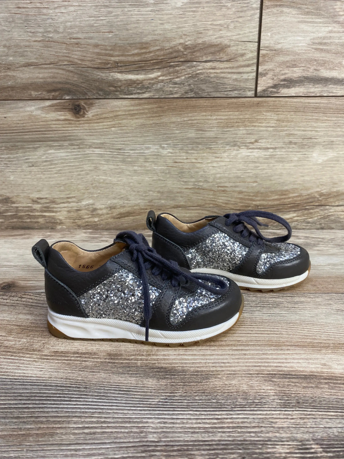 Front three-quarter view of grey Angulus glitter sneakers with silver panels, leather trim, navy laces, and white soles on wood floor