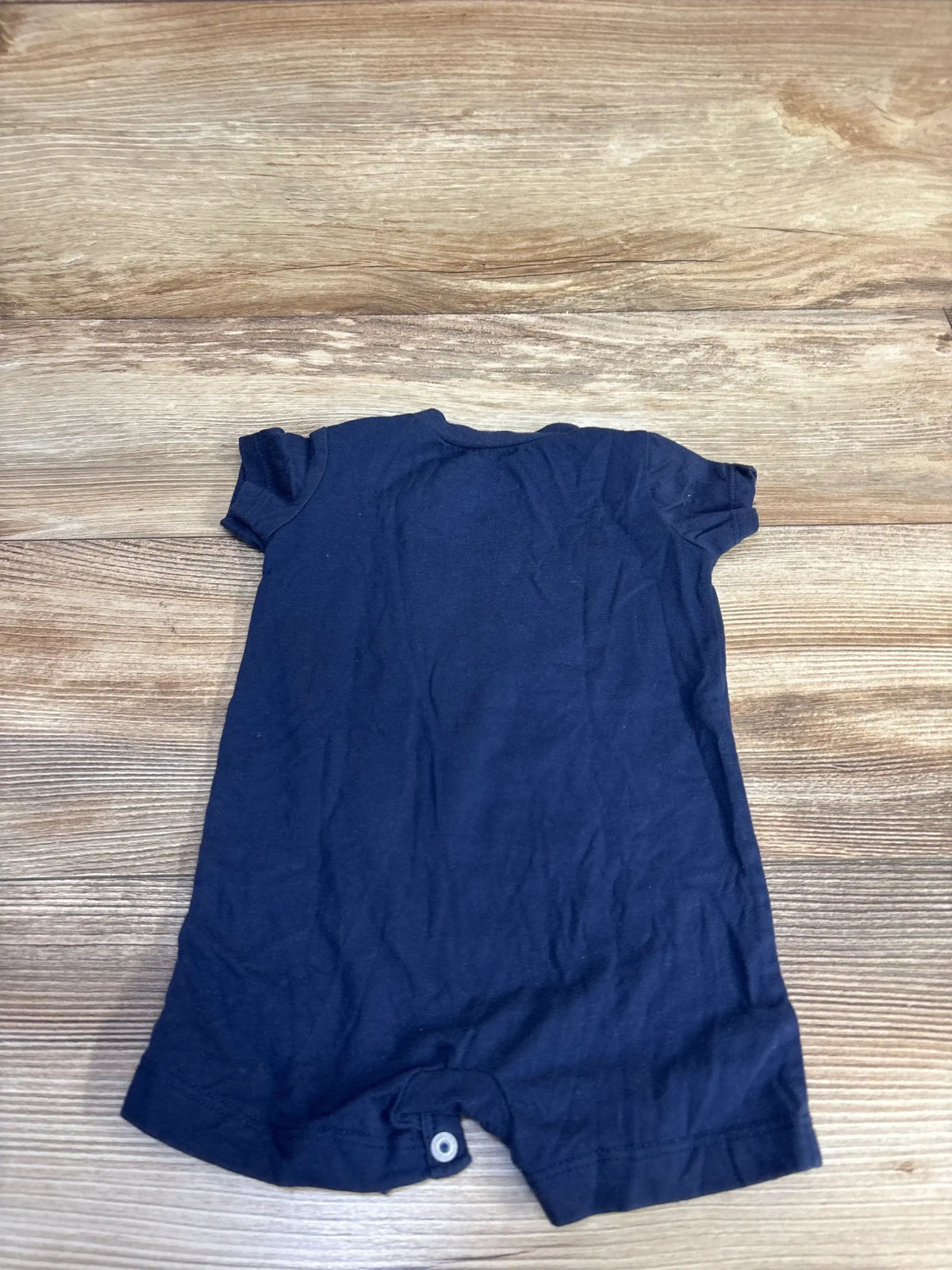 Flat lay of navy Nike shortie romper size 6 months showing snap crotch and short sleeves on wood background