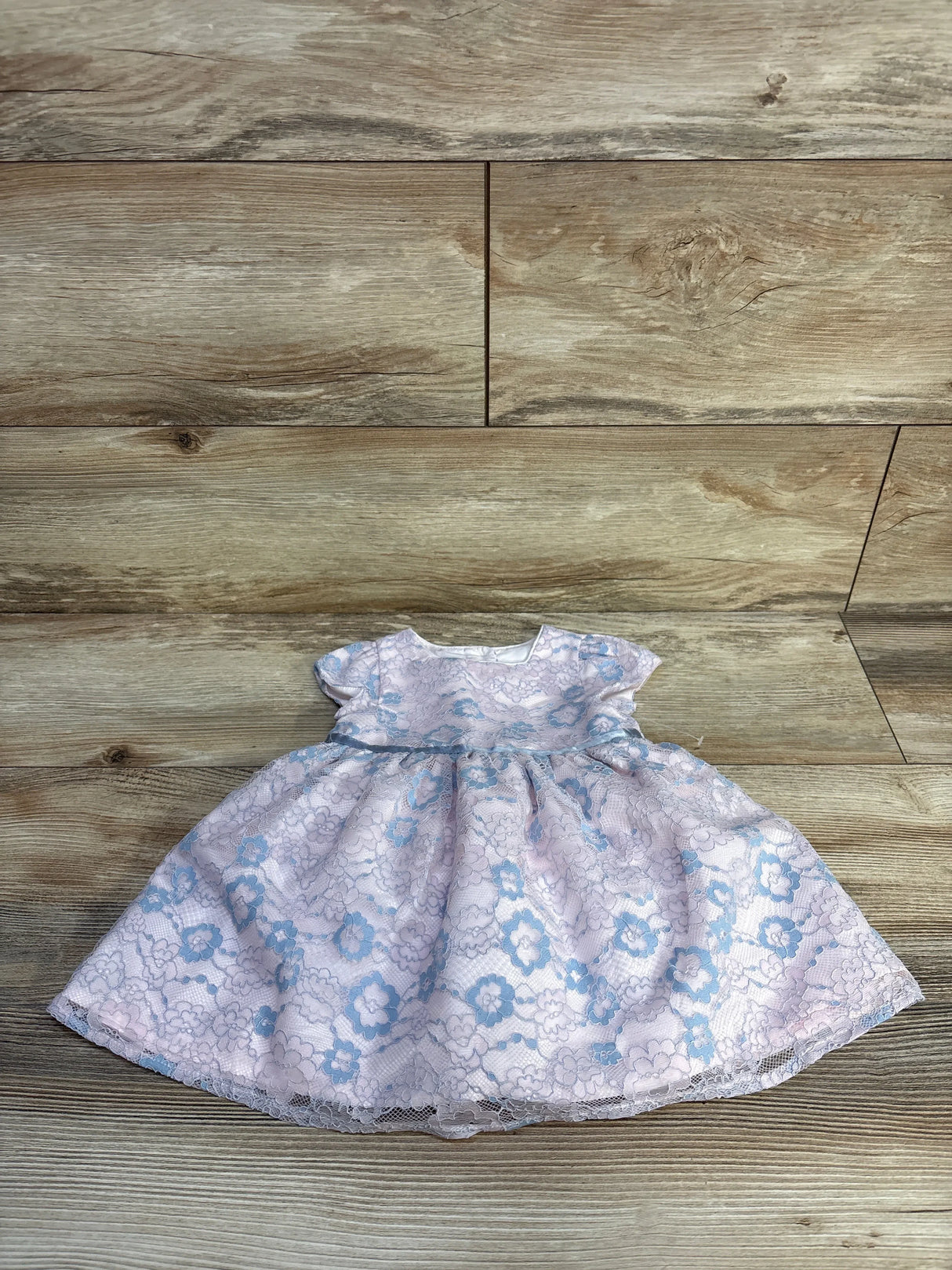 Pink baby dress with blue floral lace pattern on wooden floor