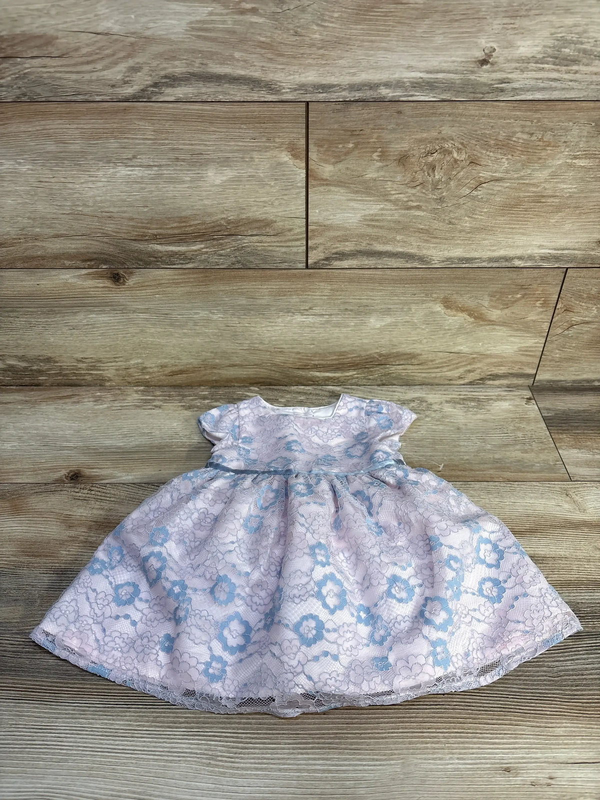 Pink baby dress with blue floral lace pattern on wooden floor