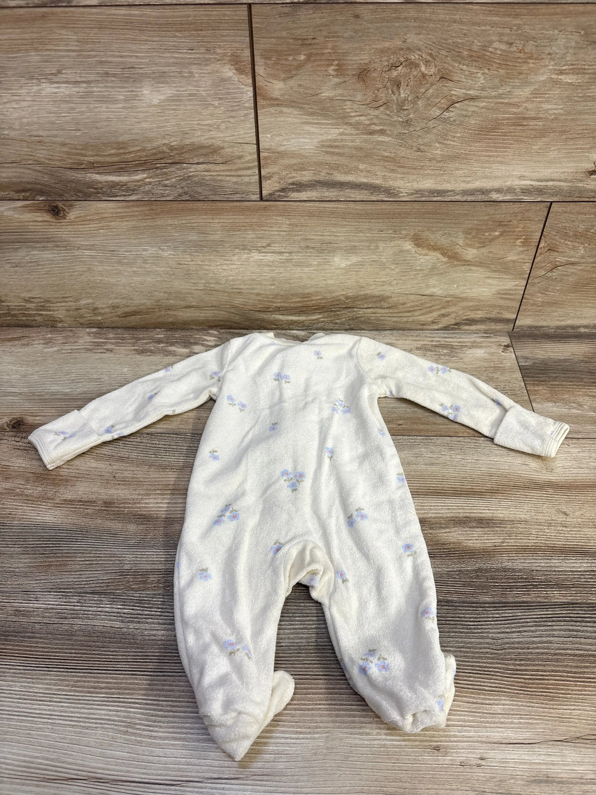Front view of Carter’s cream terry cloth sleeper showcasing floral print and footed legs on a wood floor