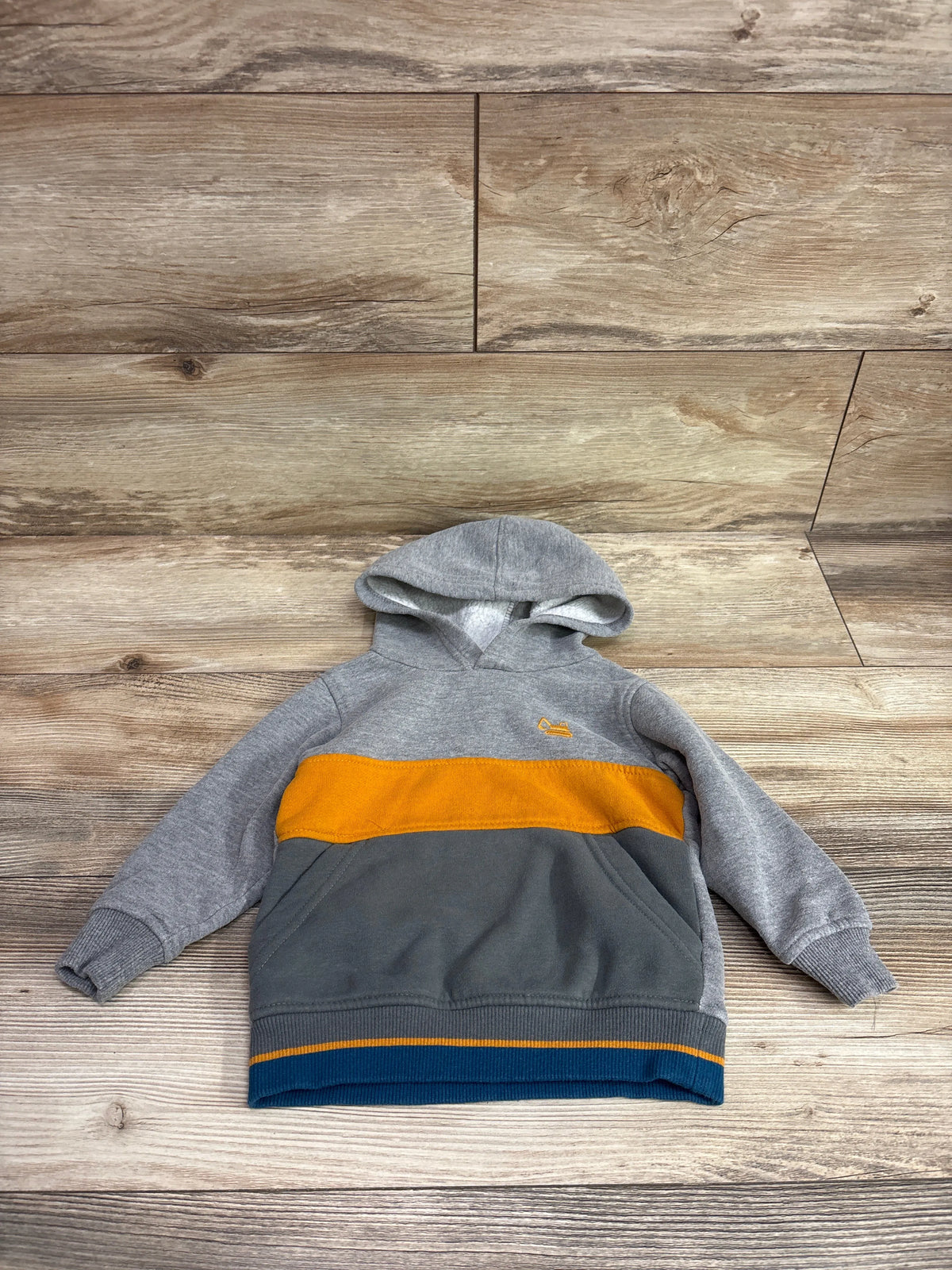 Front view of Kids Headquarters grey pullover hoodie, size 18m, showcasing orange and navy color blocking on a wood floor