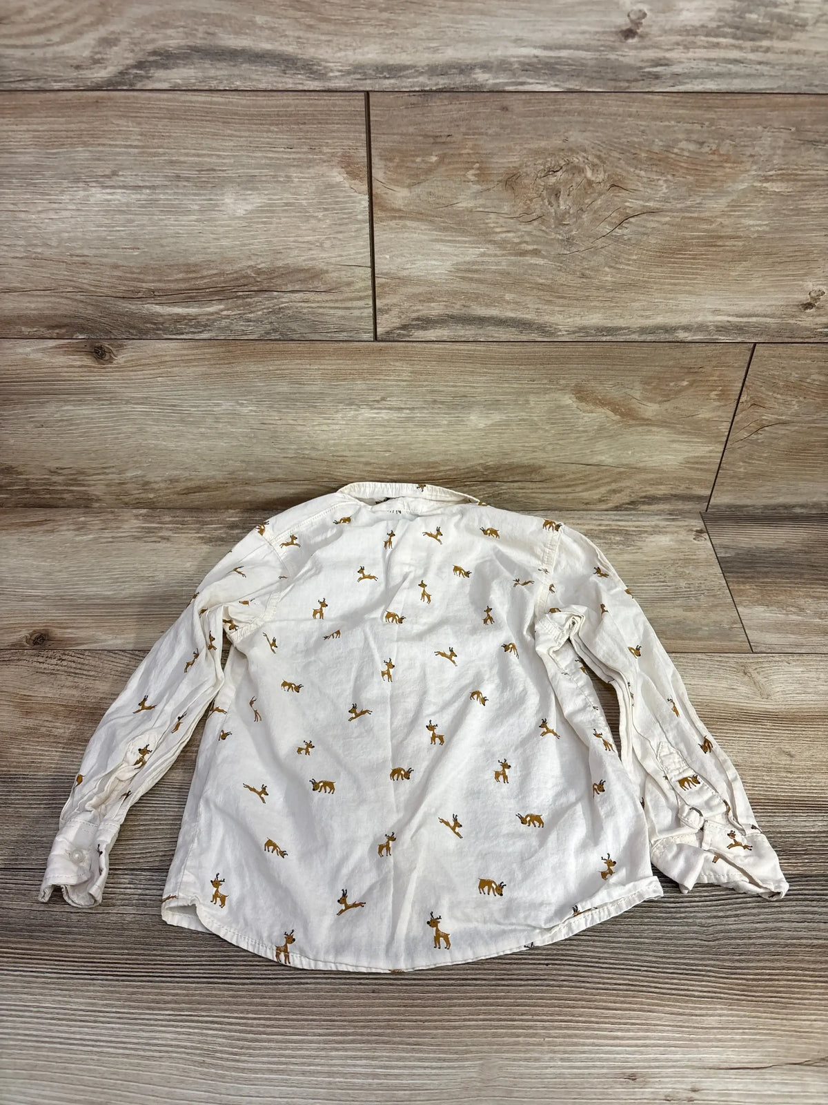 White long sleeve kids shirt with brown deer print, laid flat on wood floor