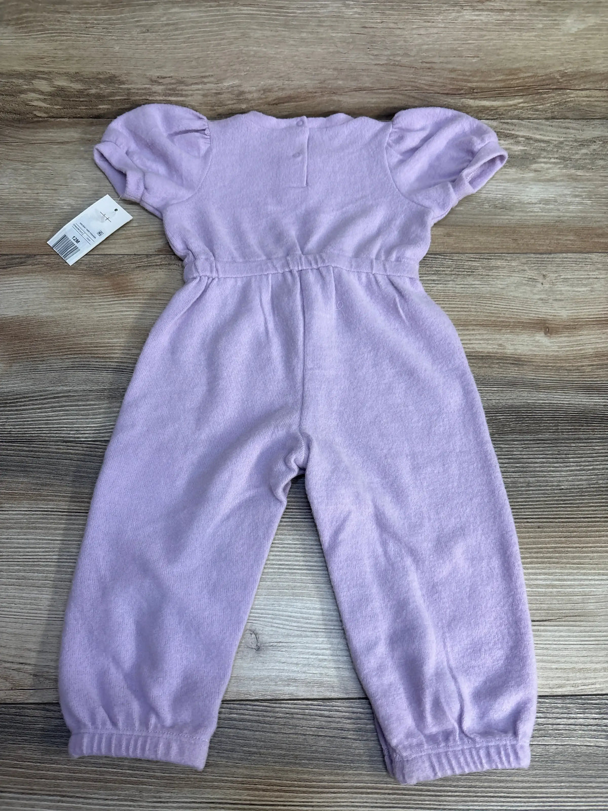 Flat lay of purple short-sleeve baby jumpsuit (12 months) showing puff sleeves, elastic waist and cuffs on wood background