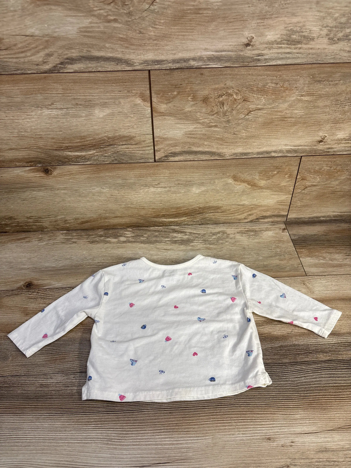 Front view of Carter’s white long-sleeve pocket shirt, size 18 months, with scattered pink and blue prints on a wood floor