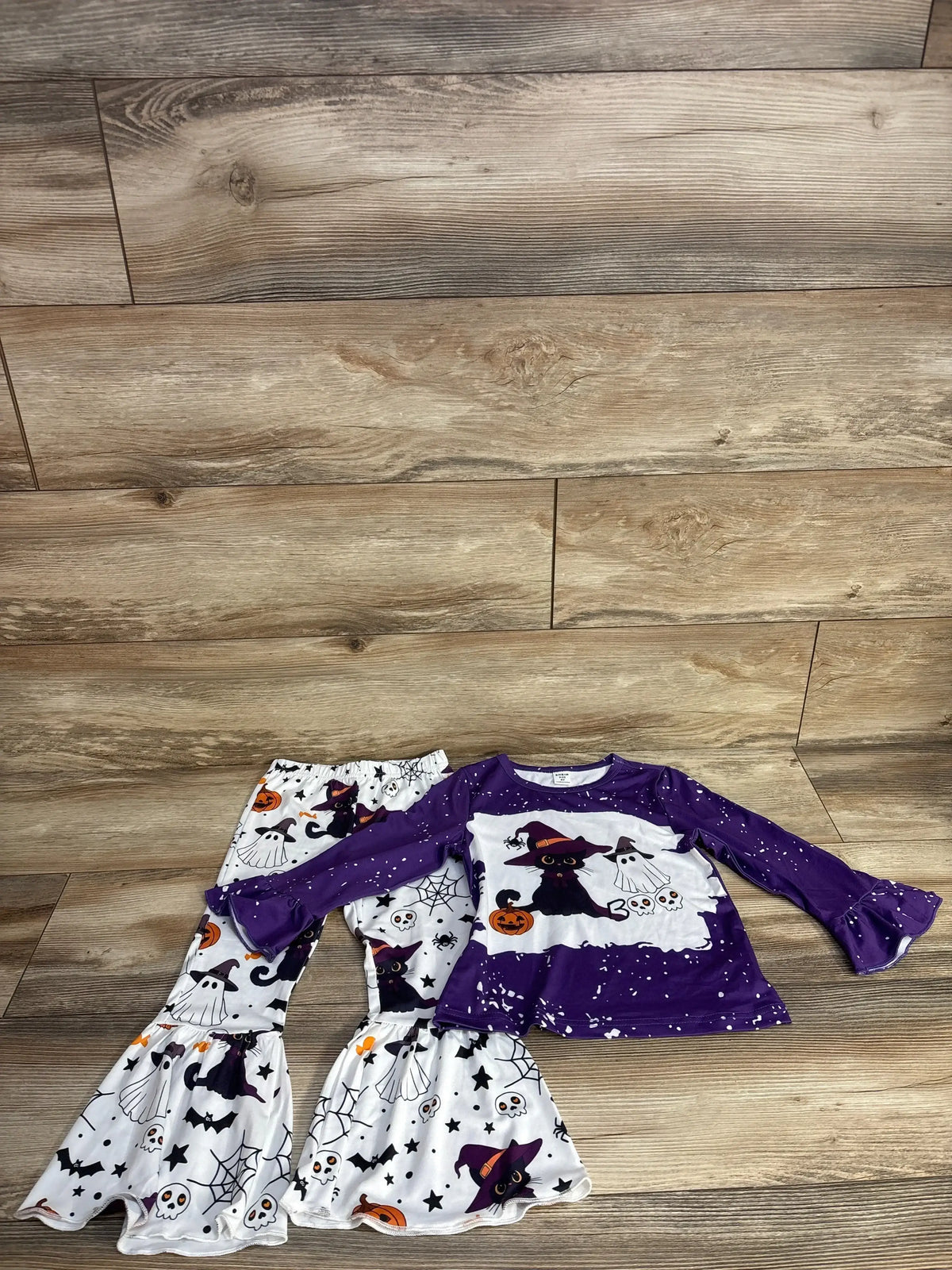 Purple and white Halloween kids outfit with witch cat, ghost, and pumpkin print on wood floor
