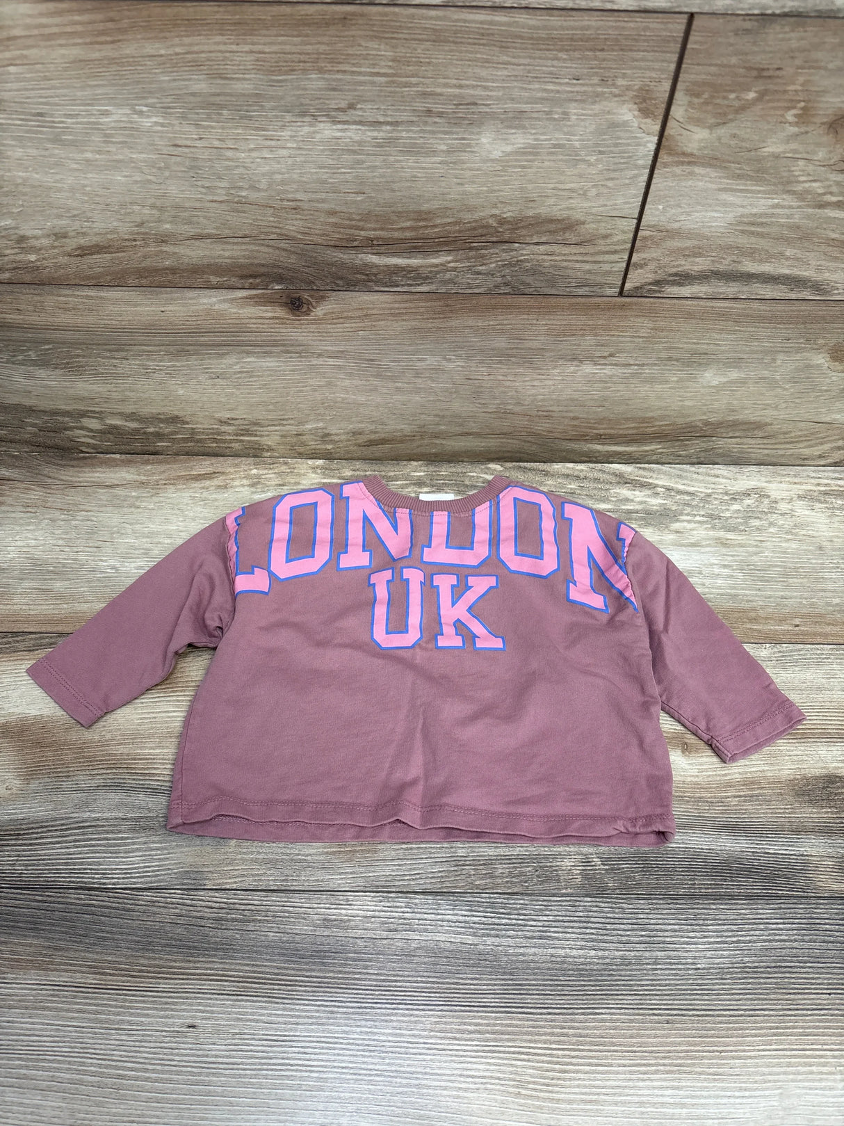 Kids mauve long sleeve shirt with 'London UK' text in pink and blue, laid on wood floor