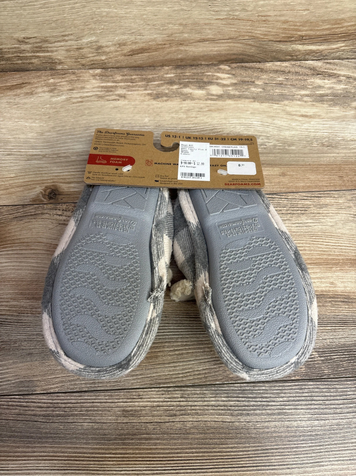 Pair of Dearfoams cream plaid memory foam slippers on wooden surface with price tag