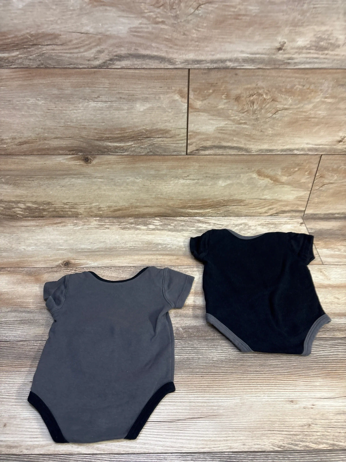 Flat lay of 2-pack Golden Knights baby bodysuits, back view showing short sleeves and contrast trim on wooden floor