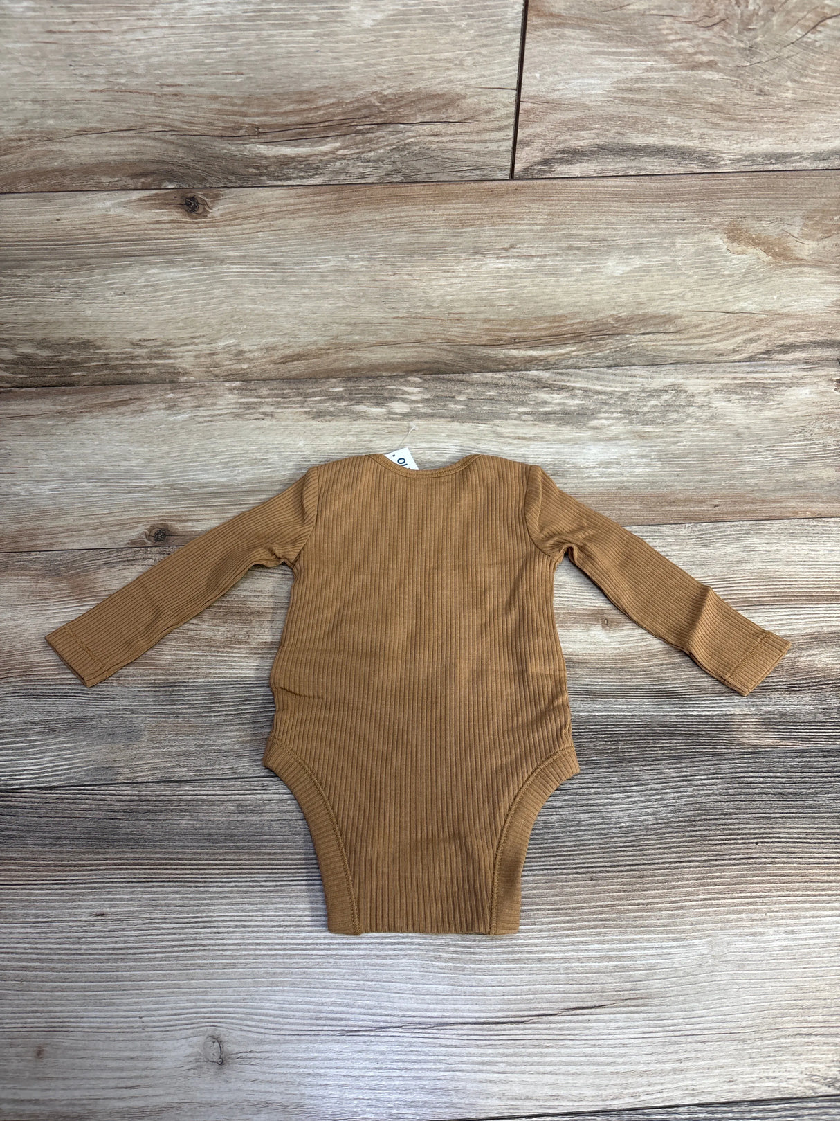 Brown long-sleeve ribbed baby bodysuit laid flat on wooden floor, children's clothing
