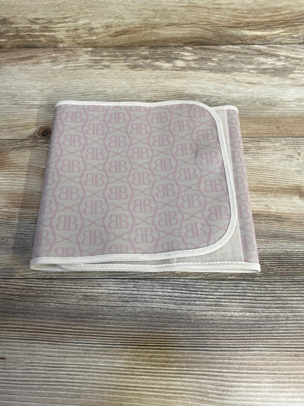 Top-down view of folded Belly Bandit postpartum wrap, beige with pink BB monogram, showing Velcro closure on wood background