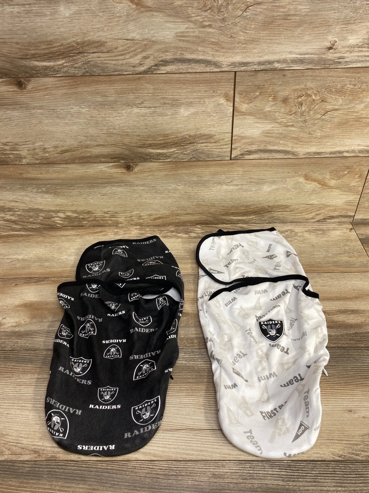 Two baby swaddle blankets with Raiders logos, one black and one white, laid on wooden floor