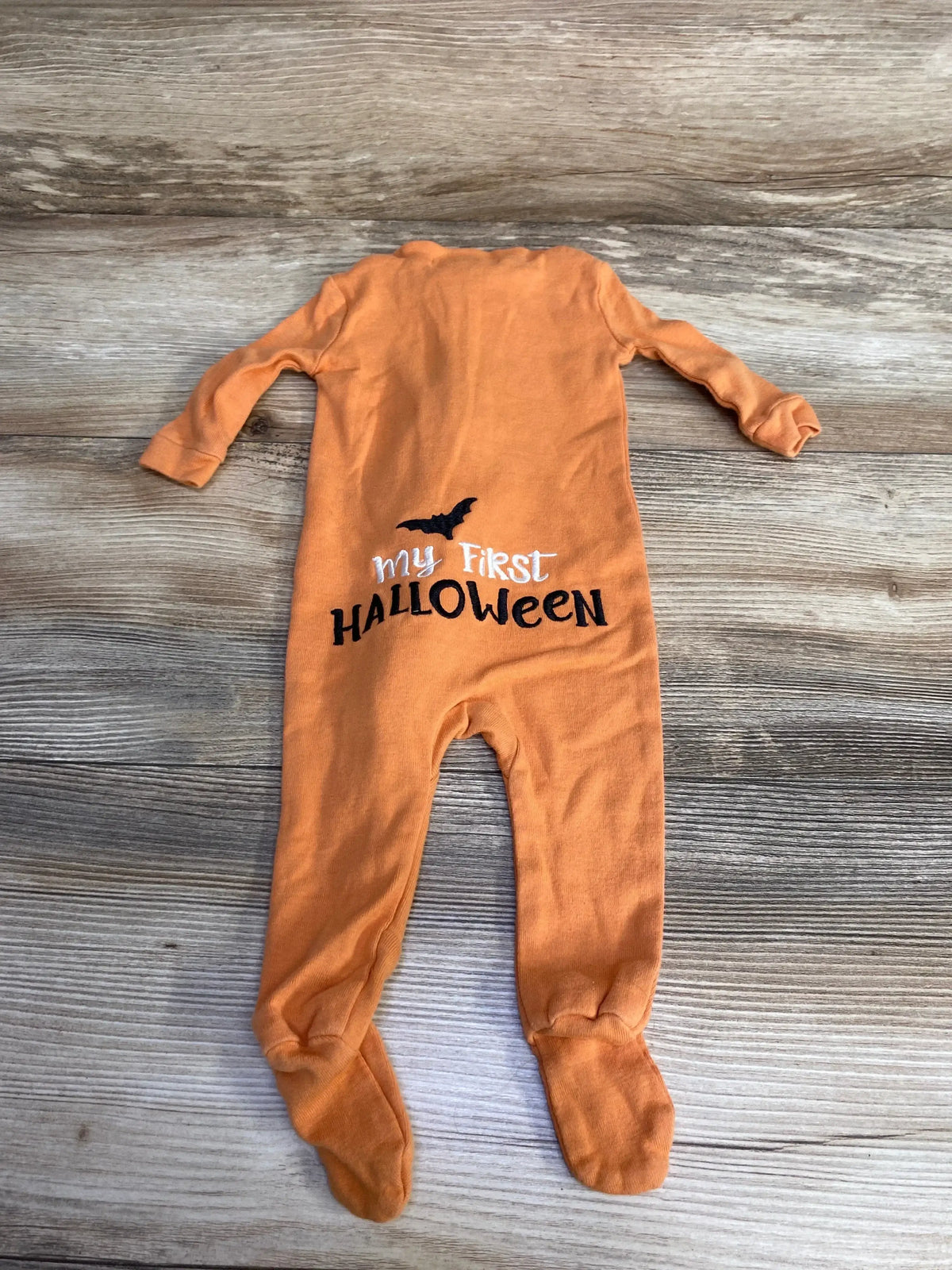 Back view of orange Pottery Barn Kids footed sleeper showing embroidered ‘My First Halloween’ text and bat on wood backdrop