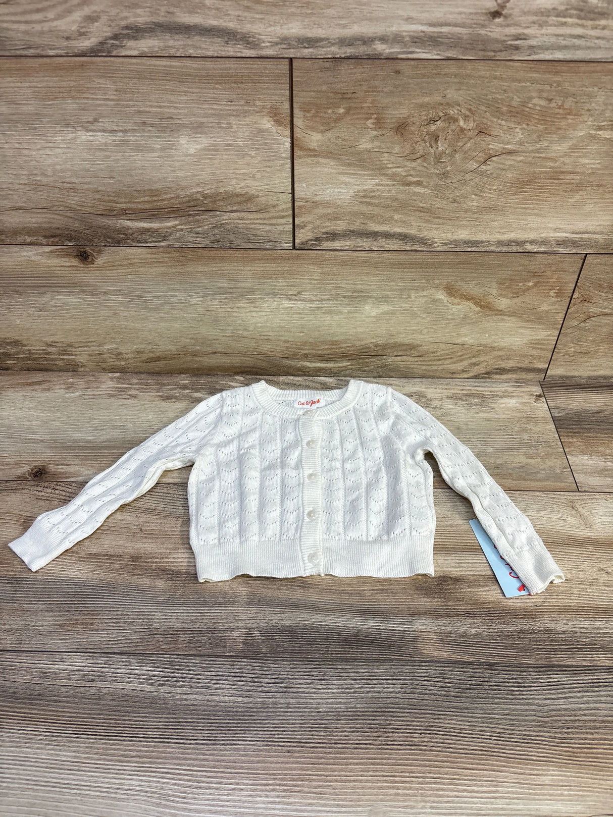 Flat lay of Cat & Jack cream pointelle button-up cardigan showing knit texture, front buttons and ribbed hem on wood floor