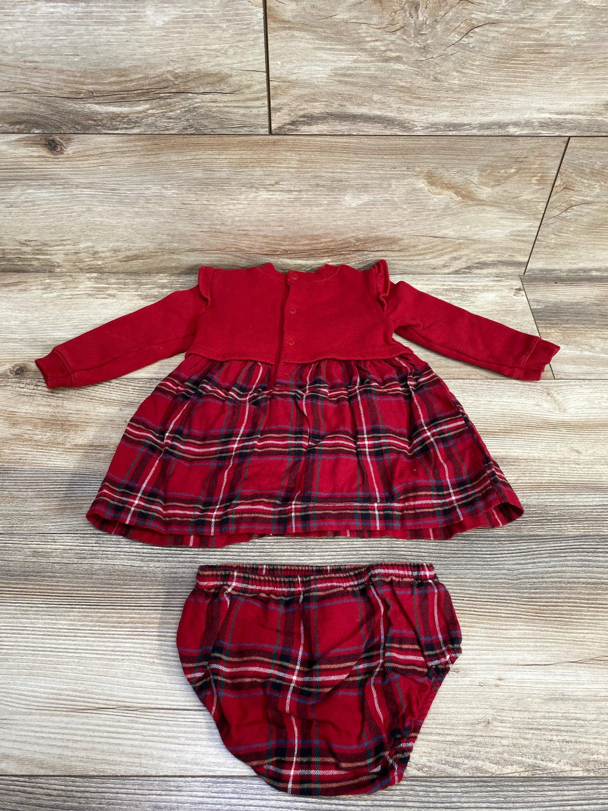 Red baby dress with long sleeves and plaid skirt paired with matching plaid diaper cover on wood floor