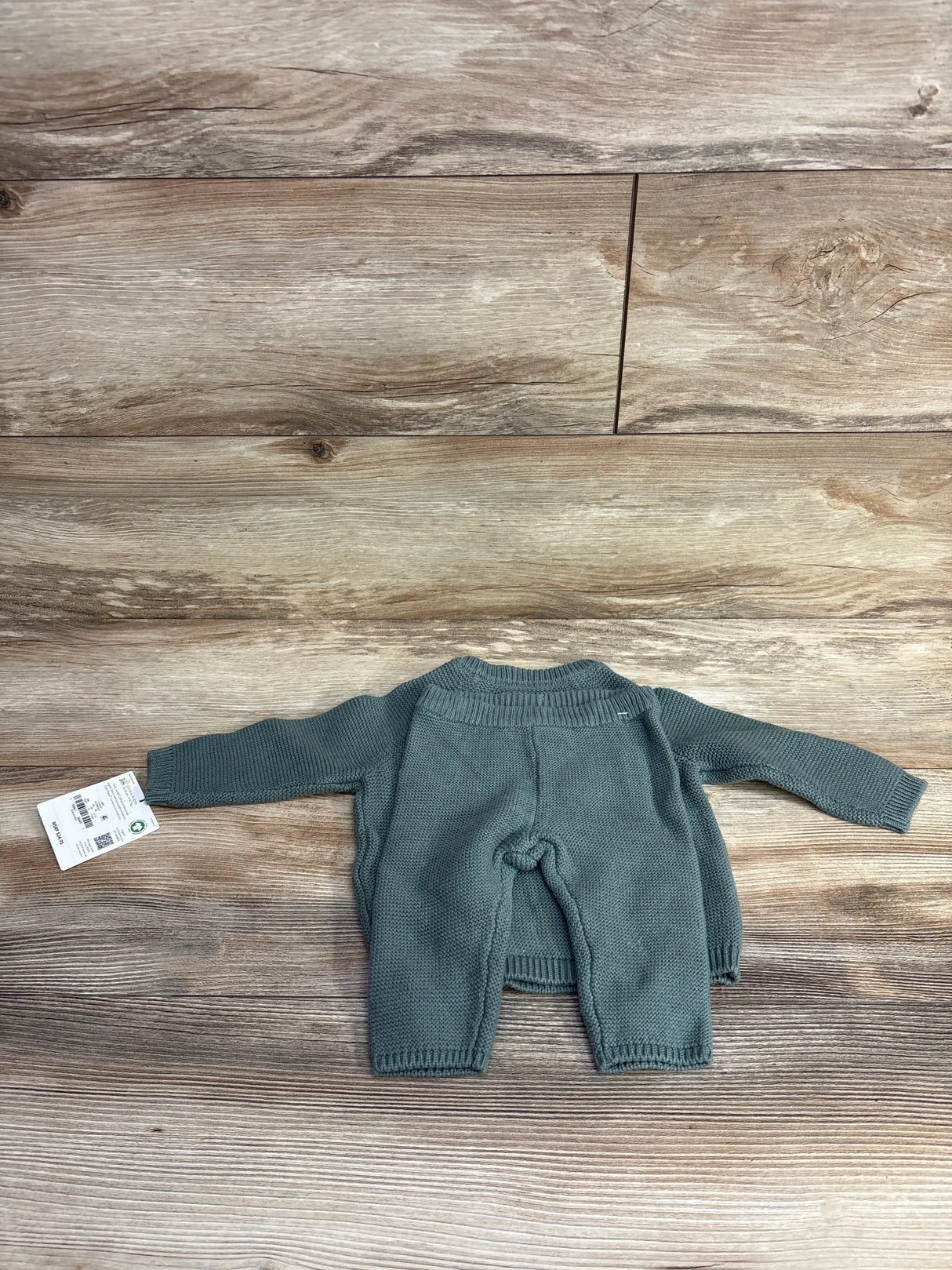 Green knit baby sweater and pants set with tag, displayed on wood background