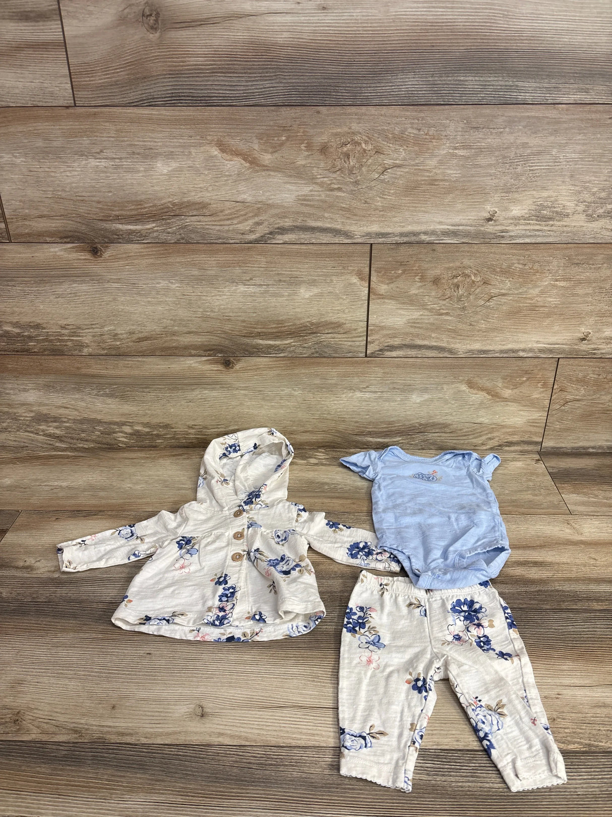 Floral baby girl outfit with hooded jacket, matching pants, and blue bodysuit on wood floor