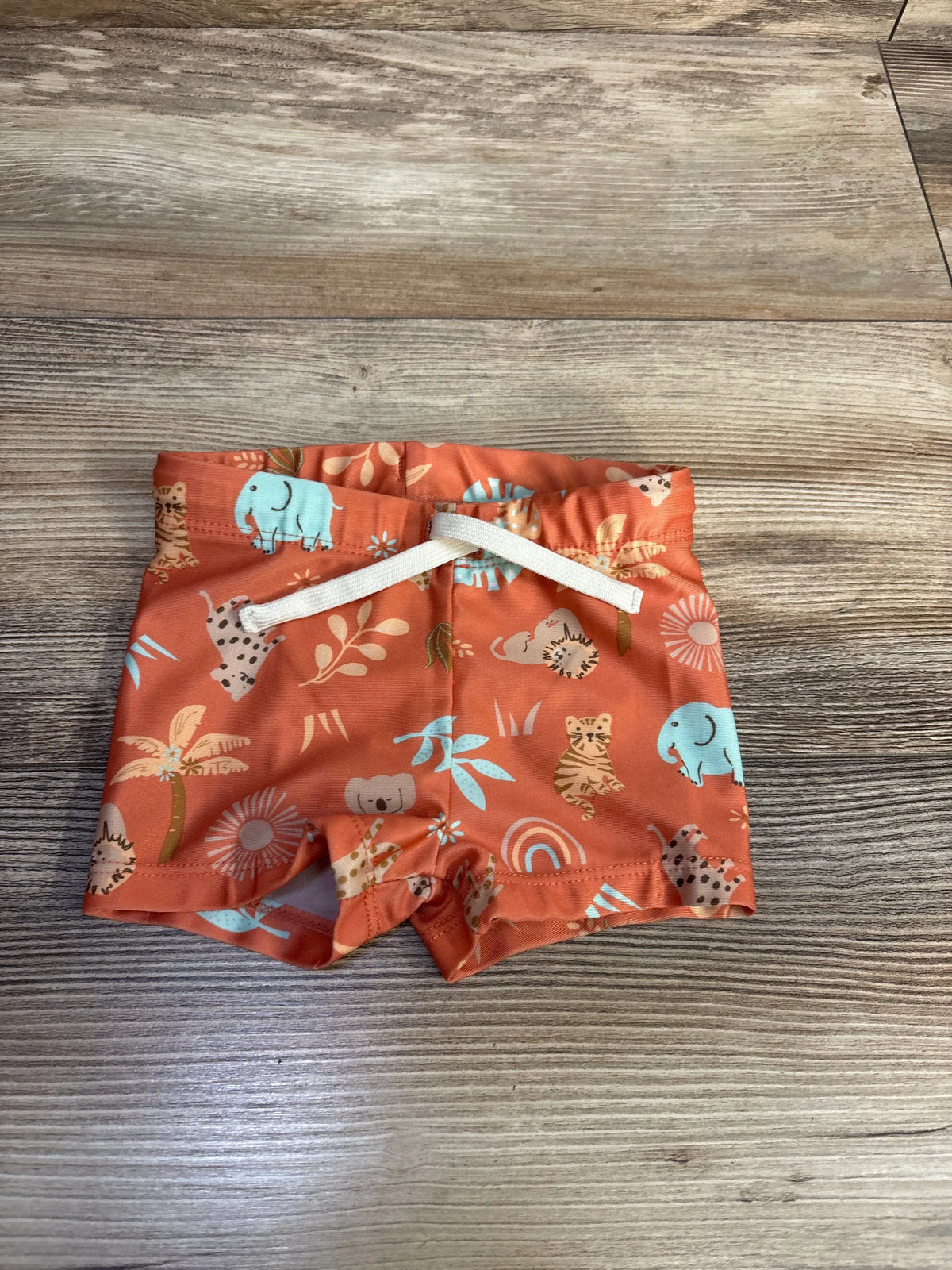 Front view of H&M orange animal print swim shorts showcasing the elastic waistband and white drawstring on a wood-grain background