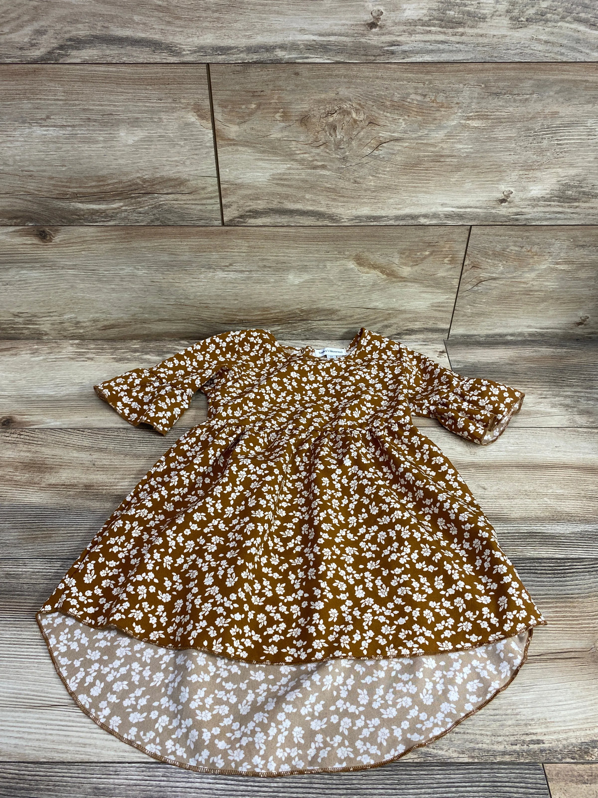 Front view of Bailey’s Blossoms floral brown dress showcasing three-quarter sleeves and a high-low hem on wood