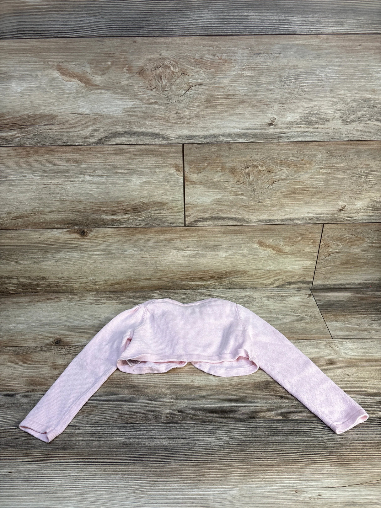 Light pink long sleeve baby bolero sweater on wooden background