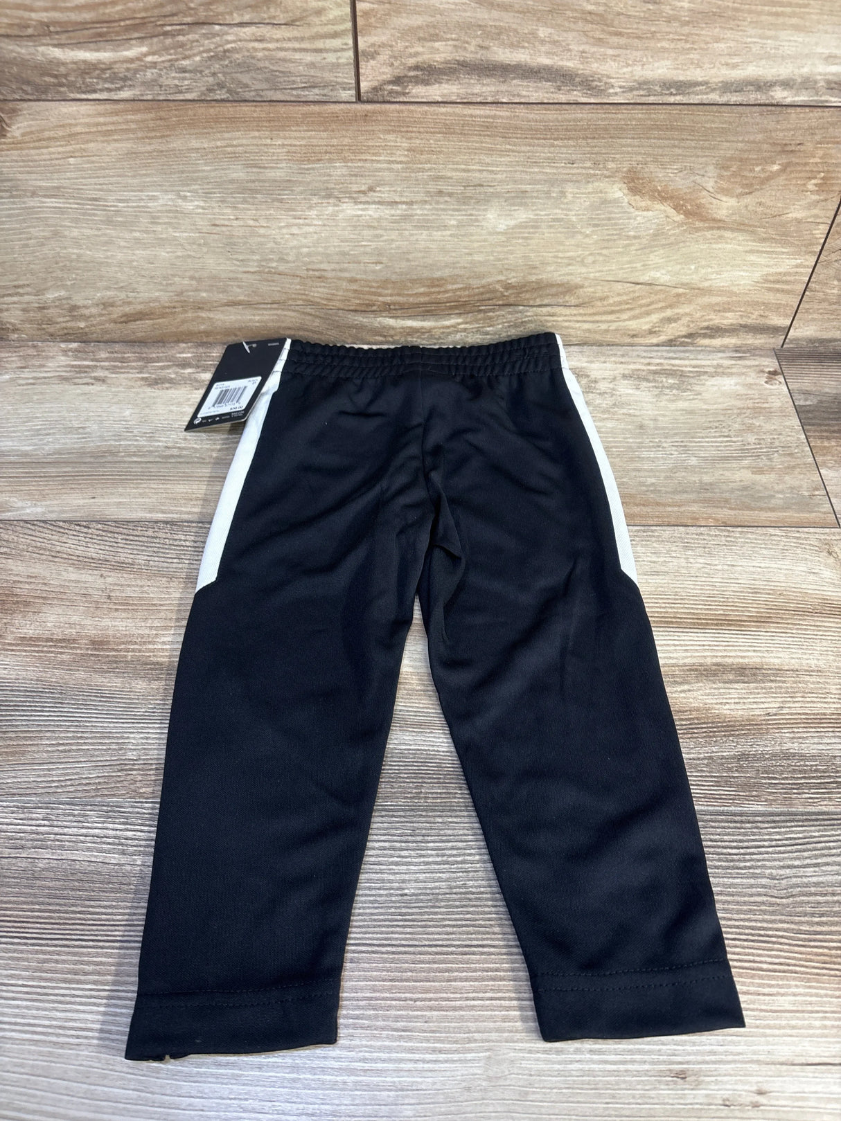 Front view of Nike toddler black active joggers size 2T with white side stripes and elastic waistband on wood background