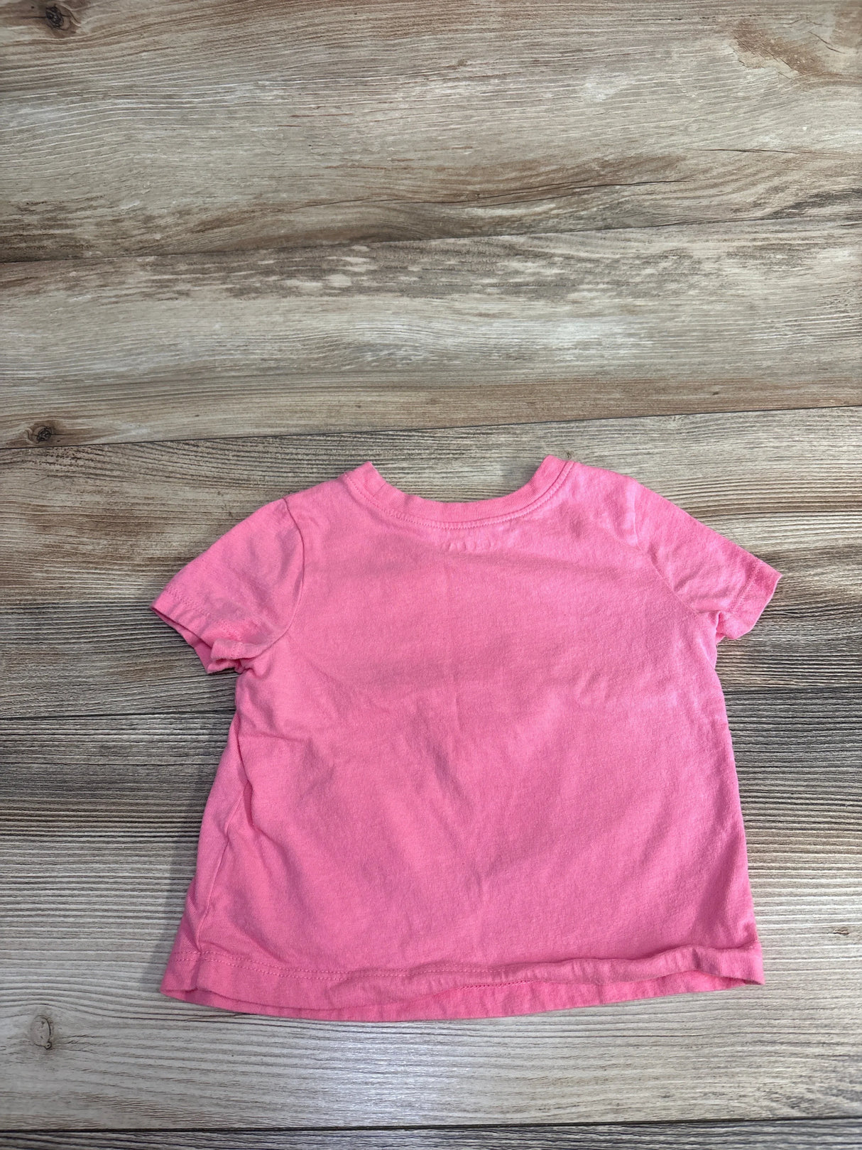 Pink short sleeve toddler t-shirt laid flat on a wood background