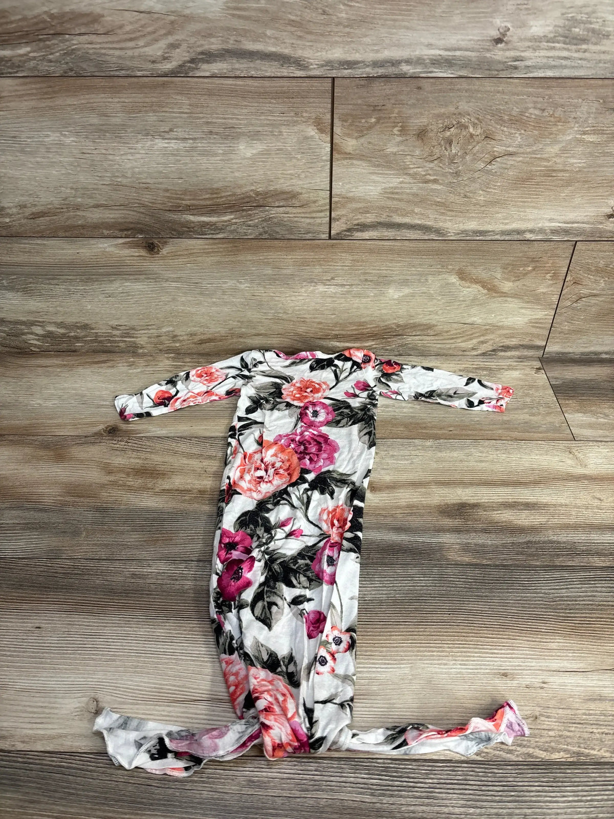 Floral newborn knotted gown with pink and peach flowers on wood background.