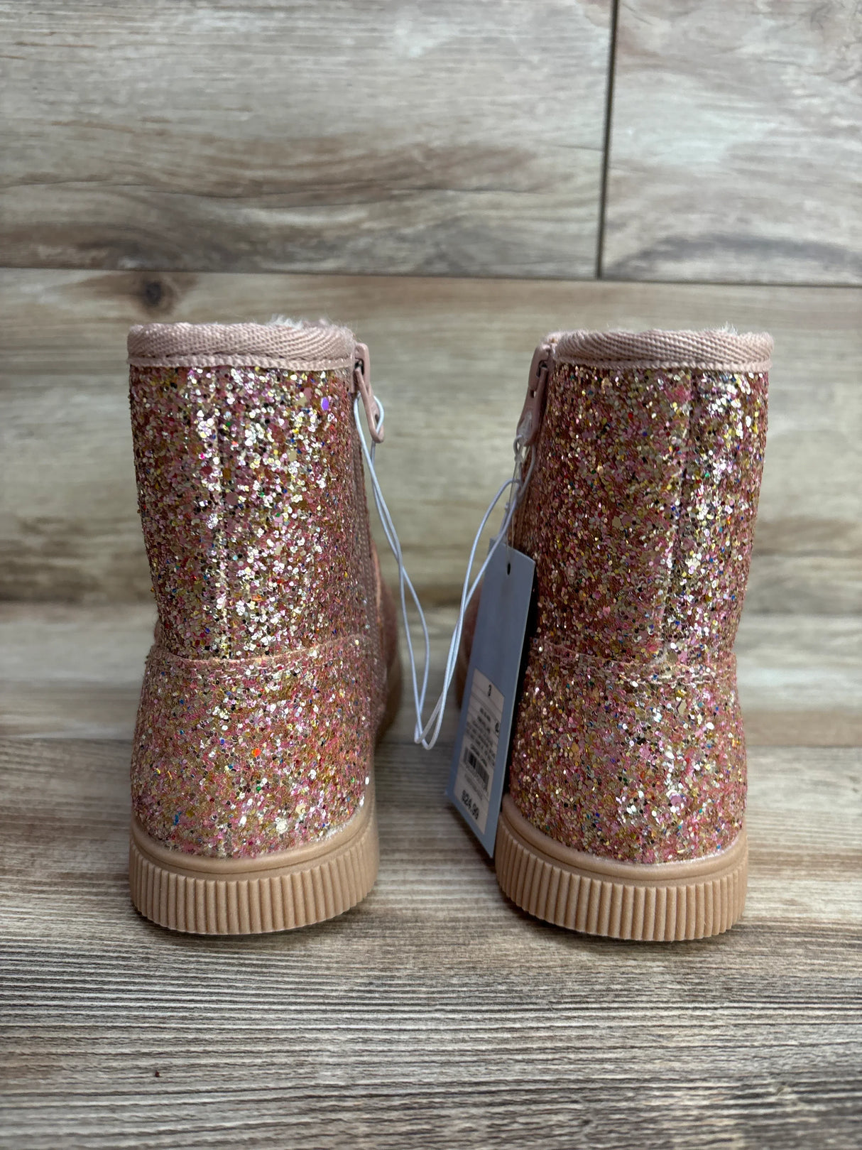 Pink glitter toddler boots with tags, rubber soles on wood background